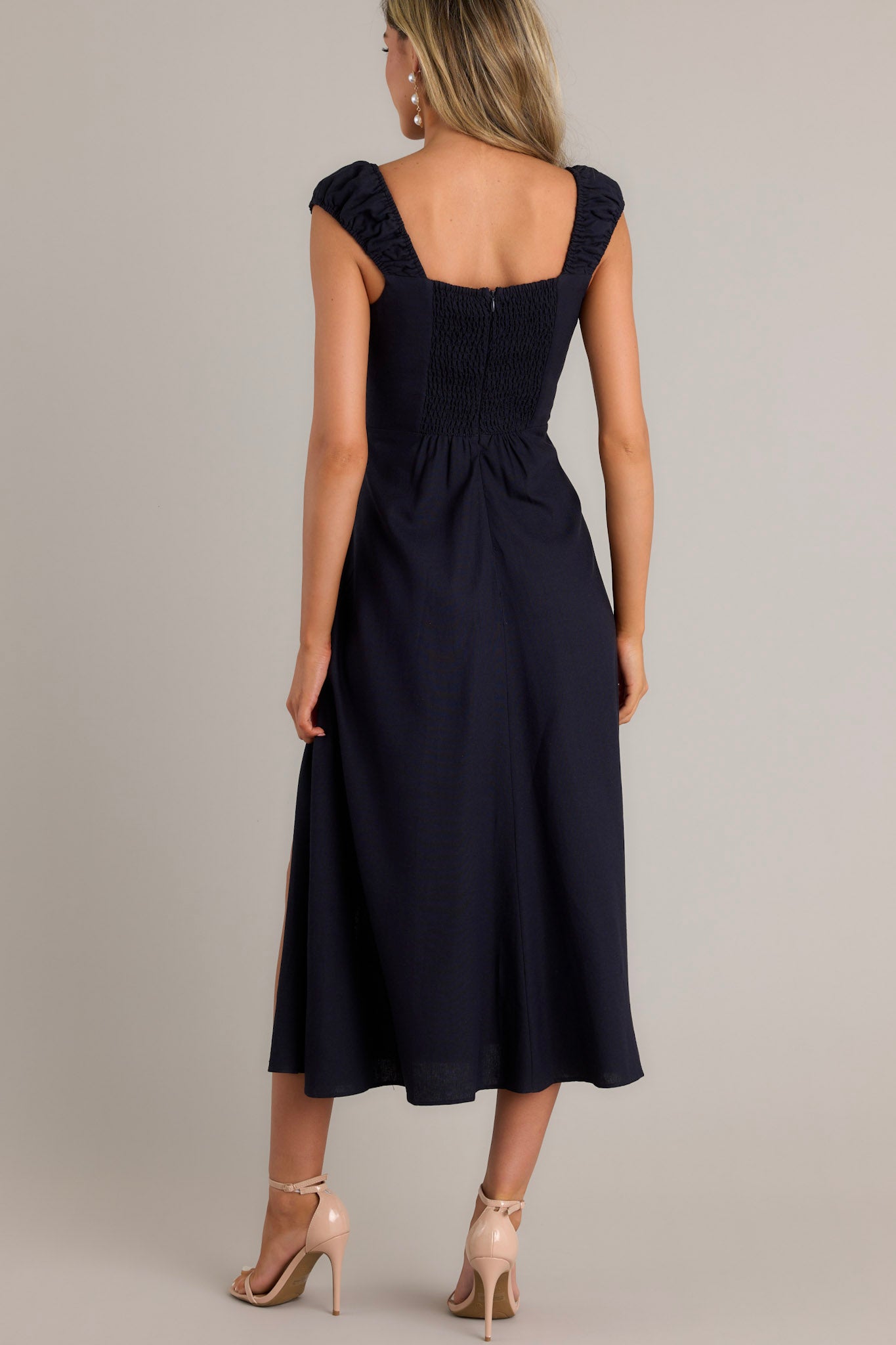 Back view of a navy midi dress highlighting the smocked section in the back, hidden zipper, and flowy skirt.