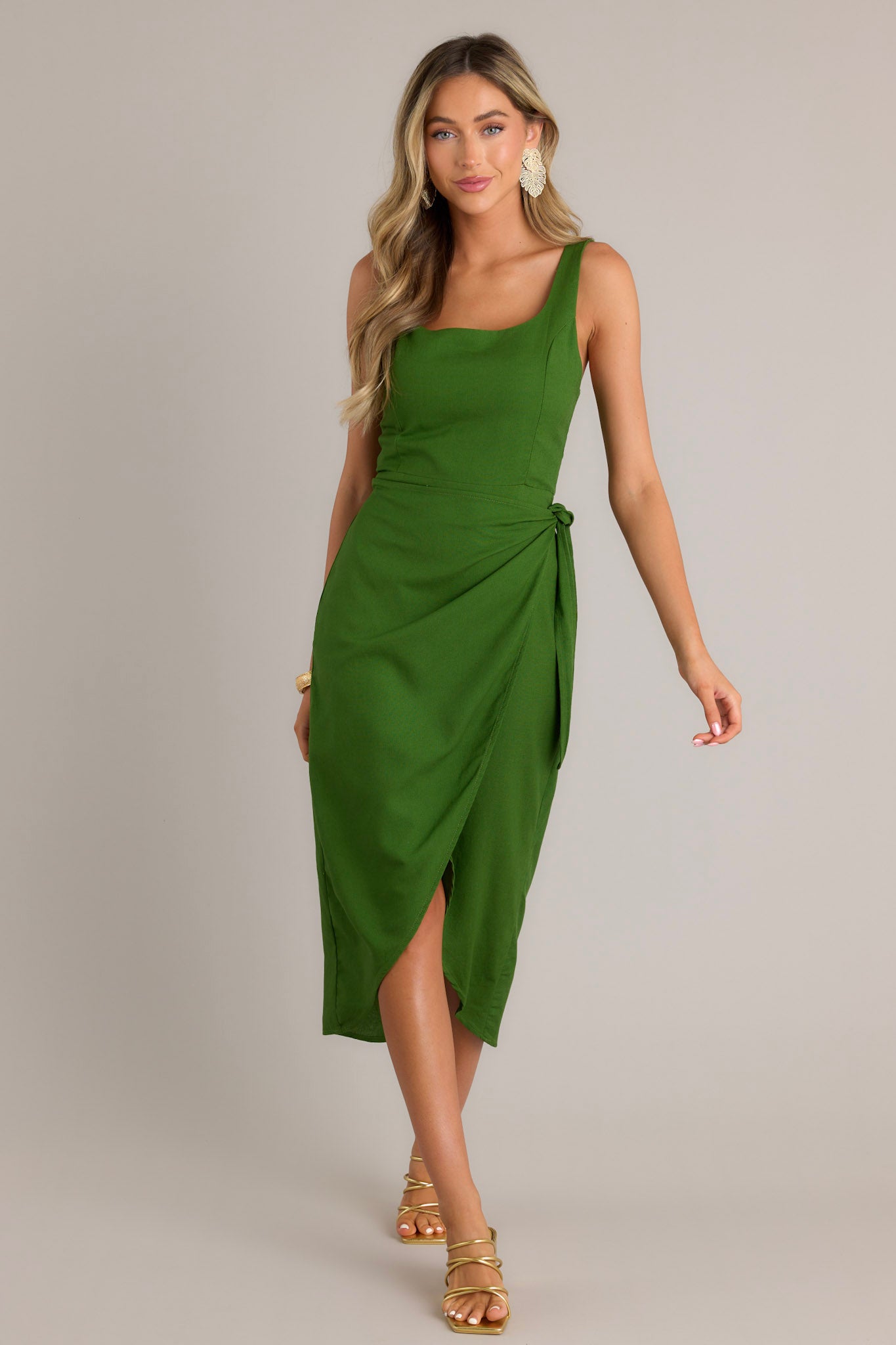 Full length view of a green midi dress with a square neckline, thick straps, a smocked back insert, a discrete zipper, a self-tie wrap feature, and a front slit