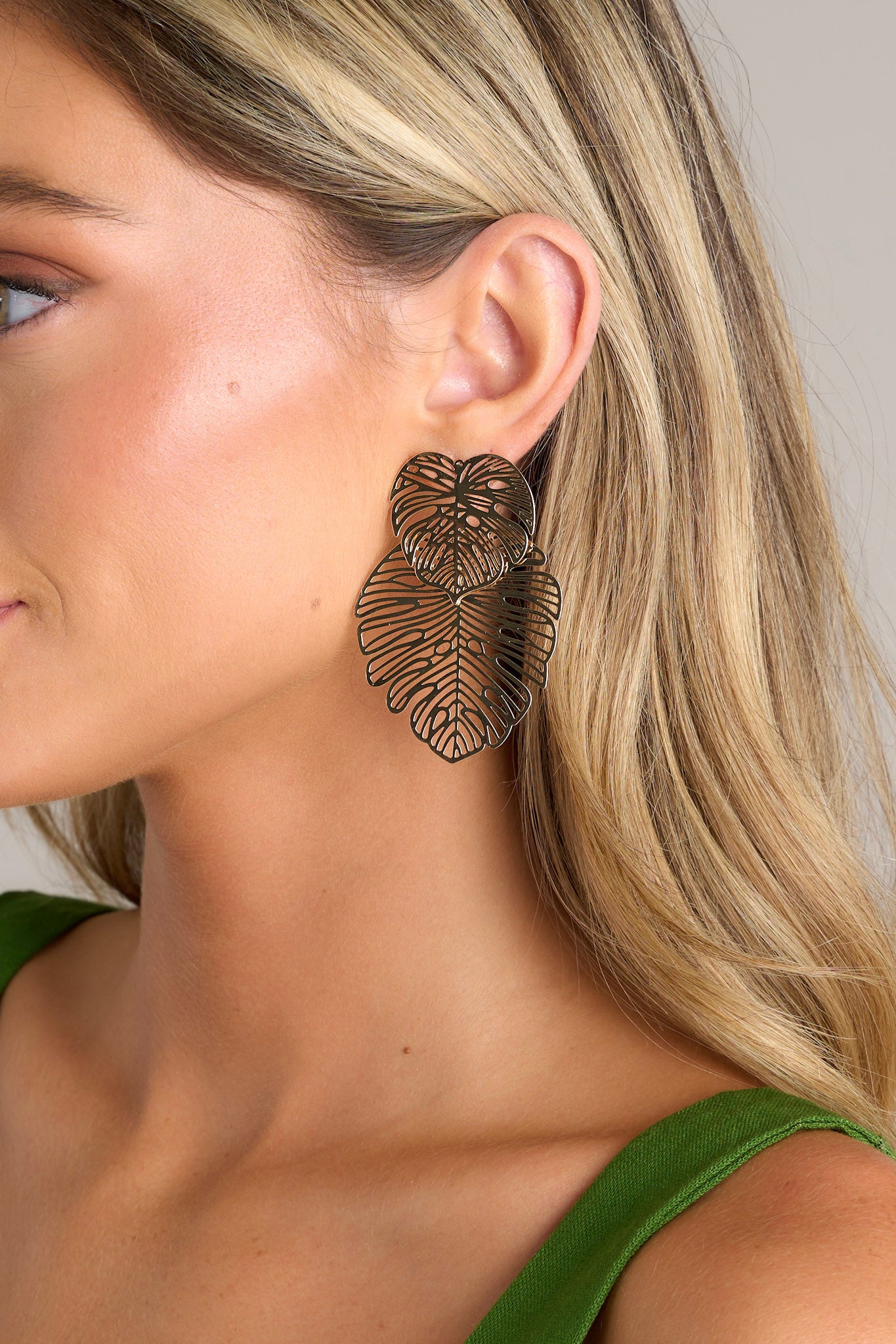 These gold earrings feature a layered transparent monstera leaf design, a lightweight material, and secure post backings.