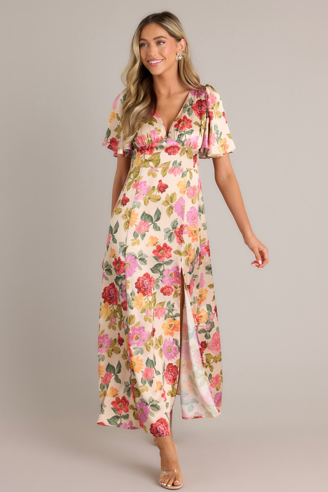 This maxi dress features a deep V-neckline, flutter sleeves, a fitted waist, A-line skirt, and a warm floral print with a subtle front slit.