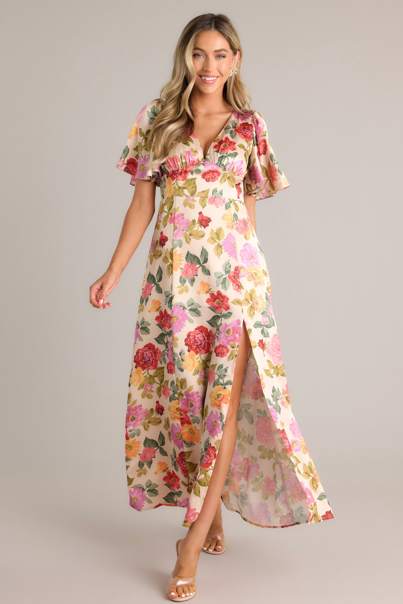 Beige floral maxi dress with a deep V-neckline, flutter sleeves, a fitted waist, A-line skirt, and a warm floral pattern throughout.