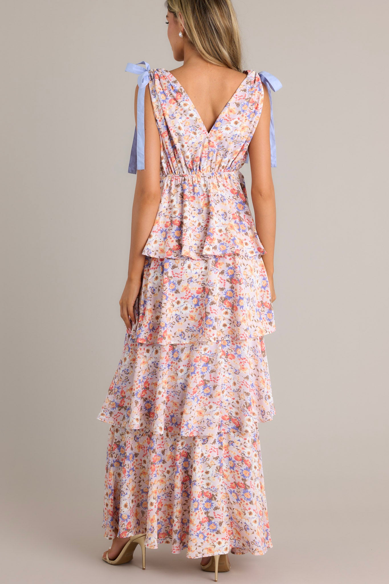 Back view of a tiered lavender ruffle maxi dress with a pastel floral pattern, showcasing the tied shoulder straps and the dress's layered back design.