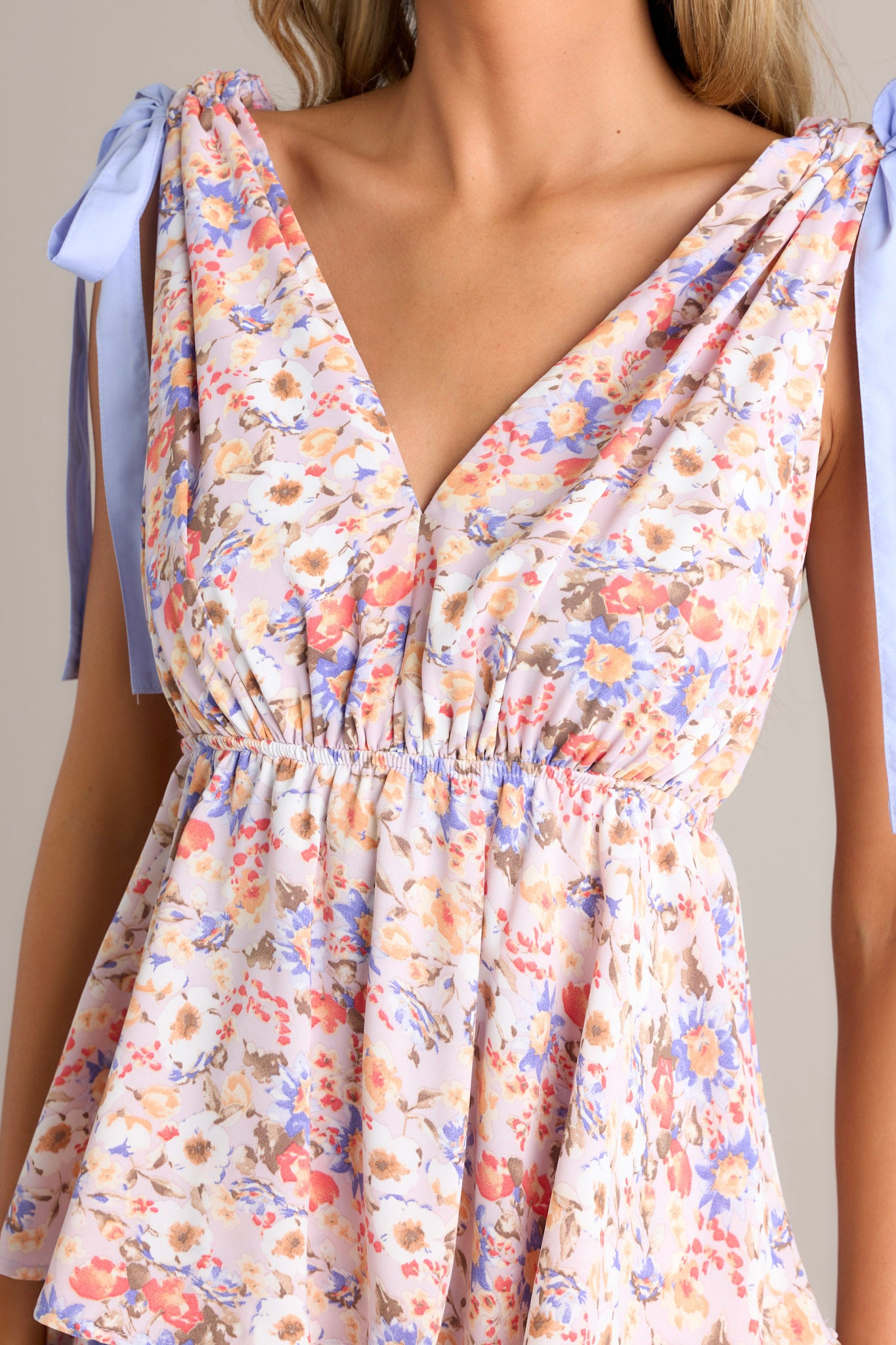 Close up view of this lavender floral dress featuring a V neckline, and self ties at the top of the shoulder.