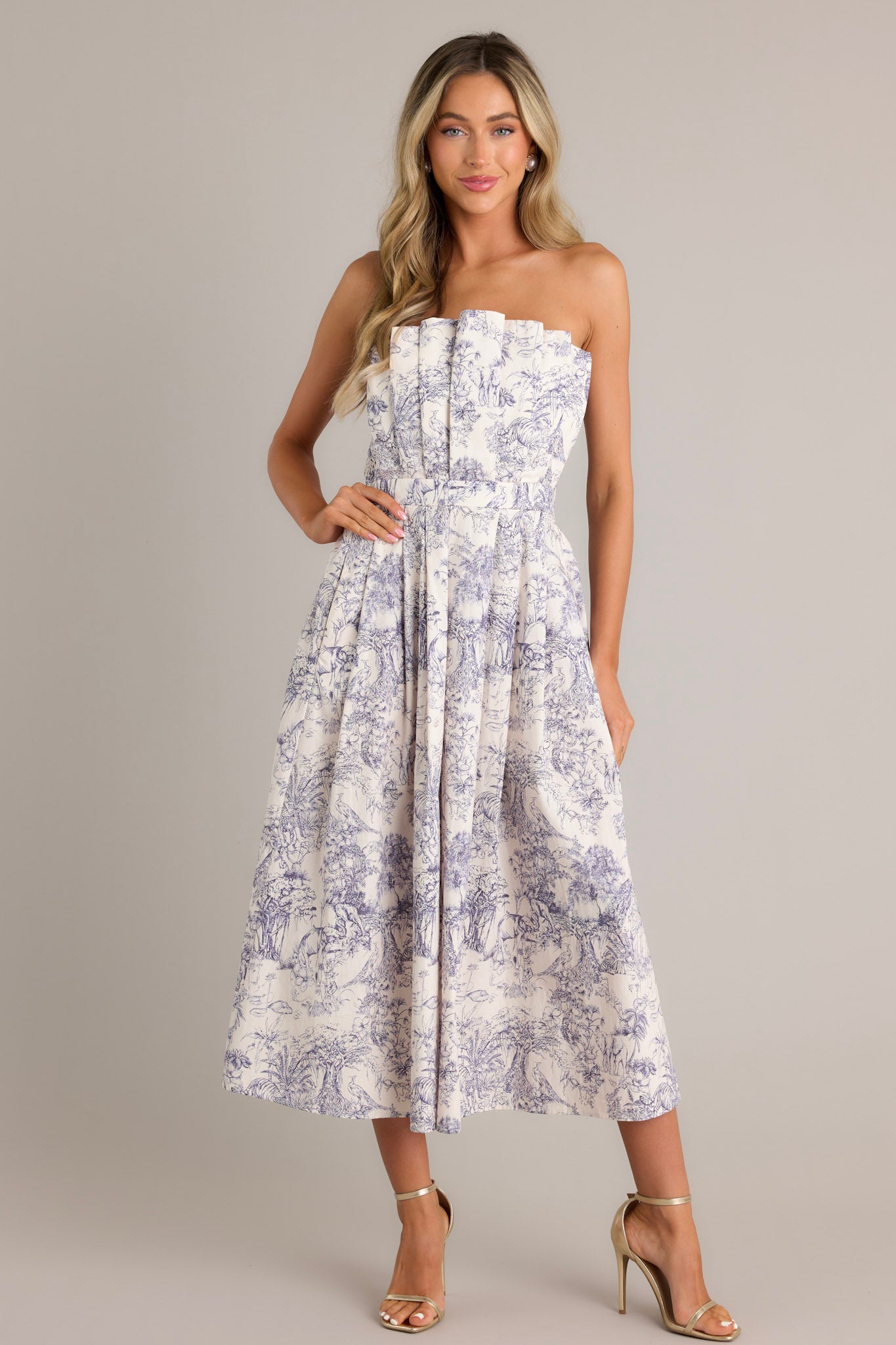 Front view of this blue toile strapless midi dress with a structured, pleated bodice, functional pockets, and a smocked back.
