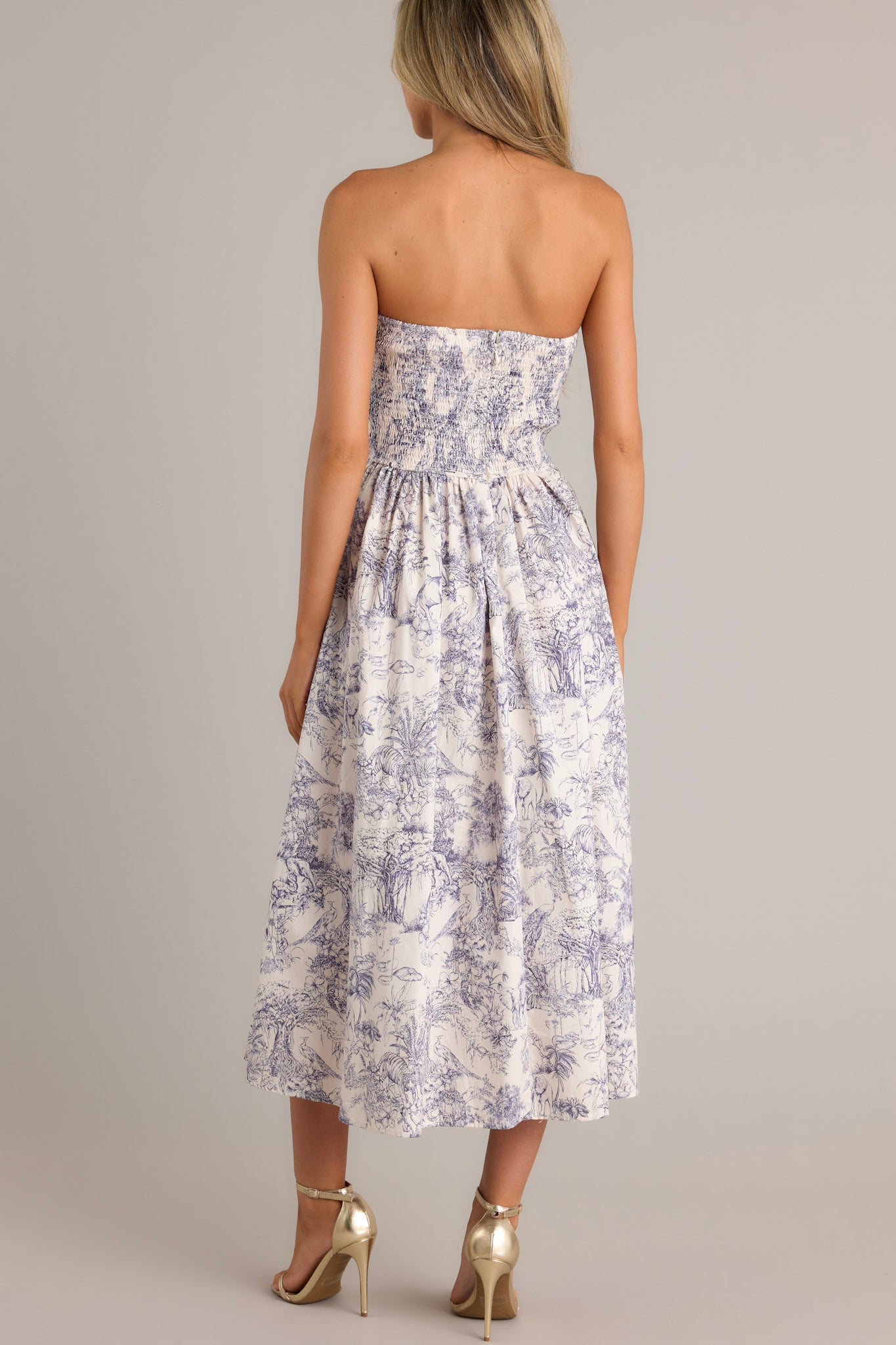 Back view of this blue toile strapless midi dress with a structured, pleated bodice, functional pockets, and a smocked back.