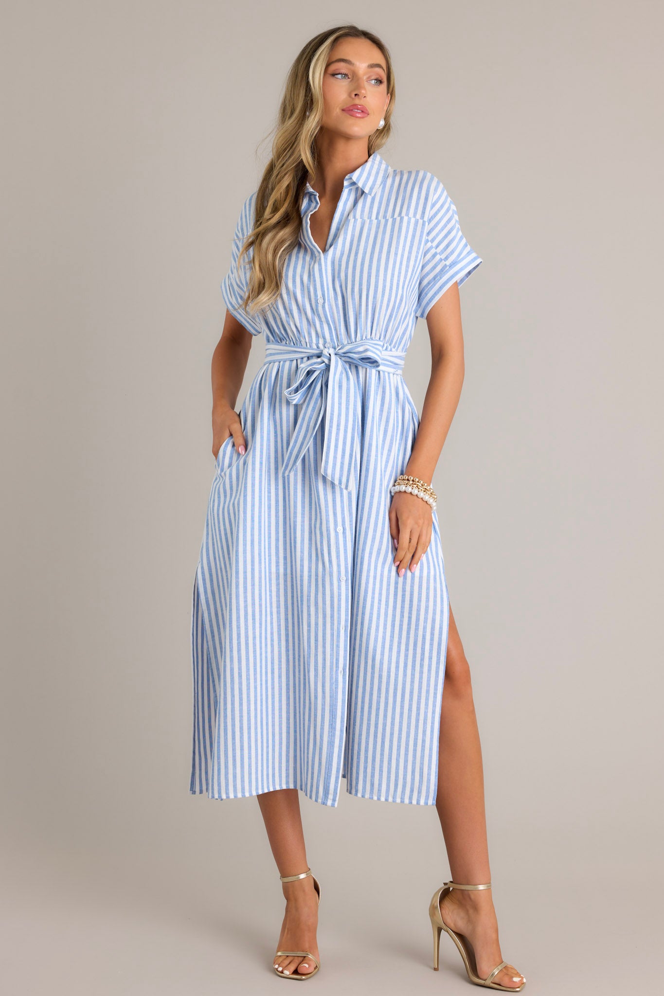Front view of this dress that features a collared neckline, a full button front, a fitted waist, a self-tie waist belt, functional pockets, two side slits, and folded short sleeves.