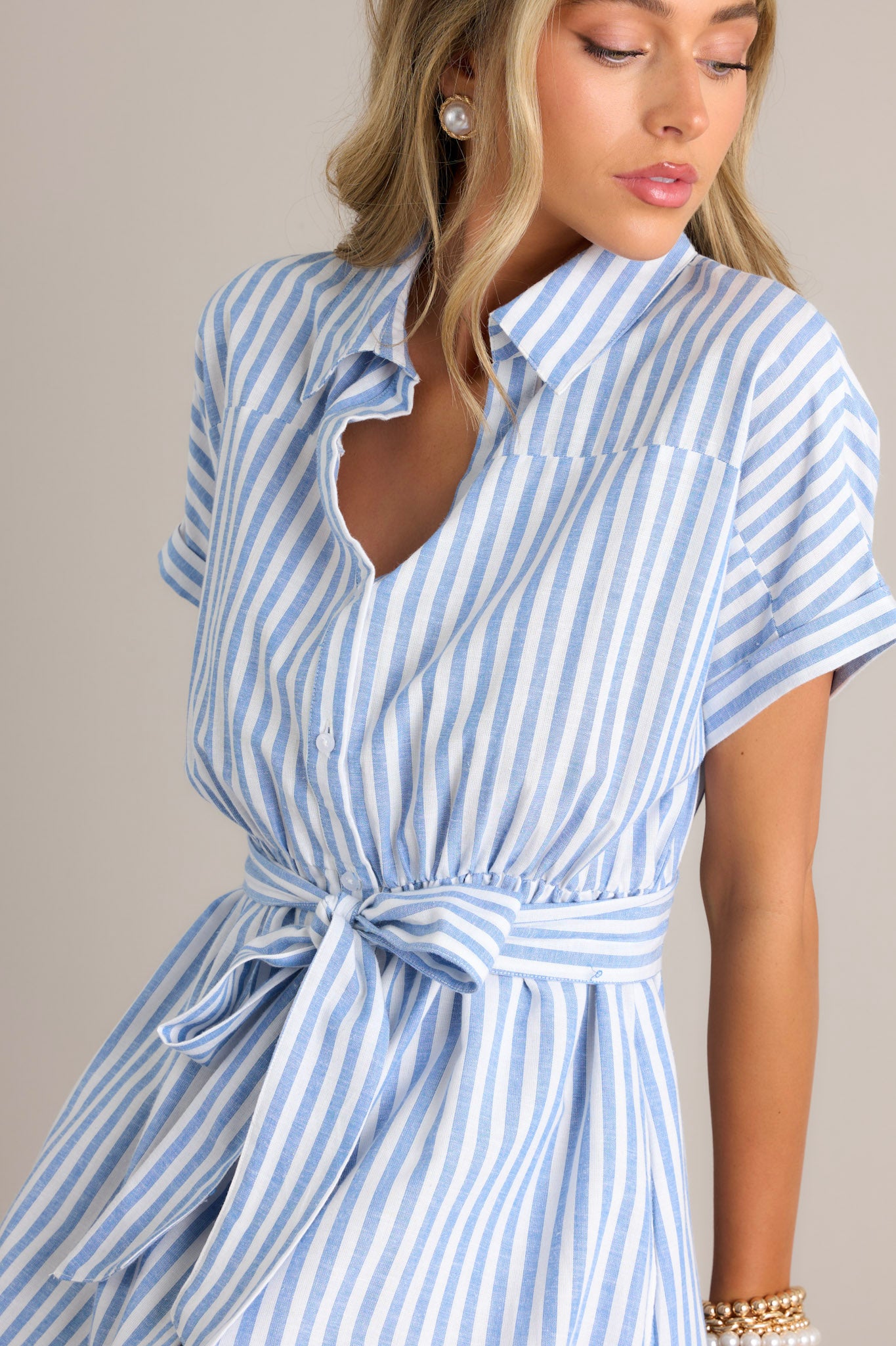 Close up view of this dress that features a collared neckline, a full button front, a fitted waist, a self-tie waist belt, functional pockets, two side slits, and folded short sleeves.