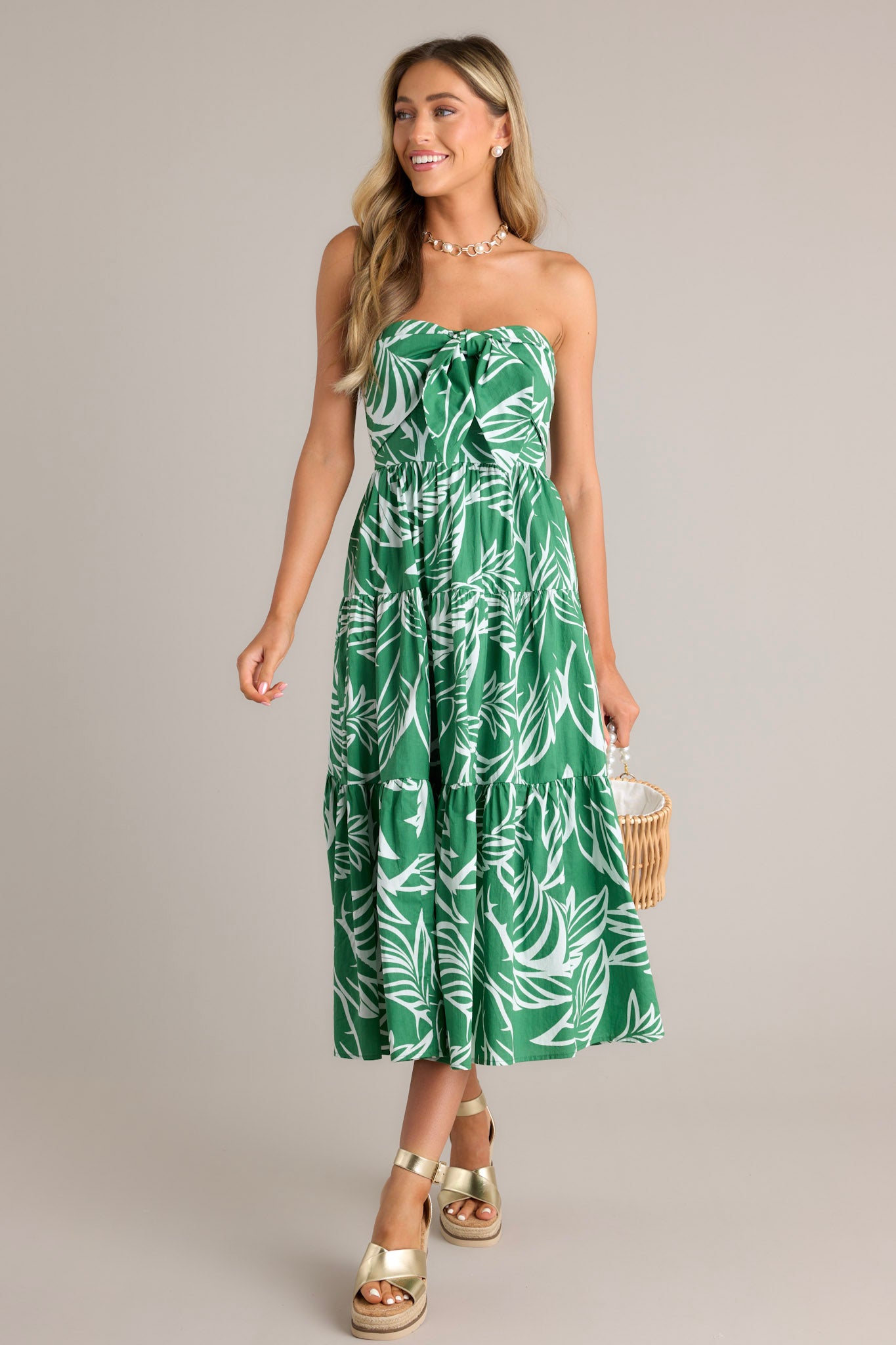 Full length view of a green midi dress with a strapless neckline, boning in the bodice, a self-tie feature, a fully smocked insert in the back, and a tiered design