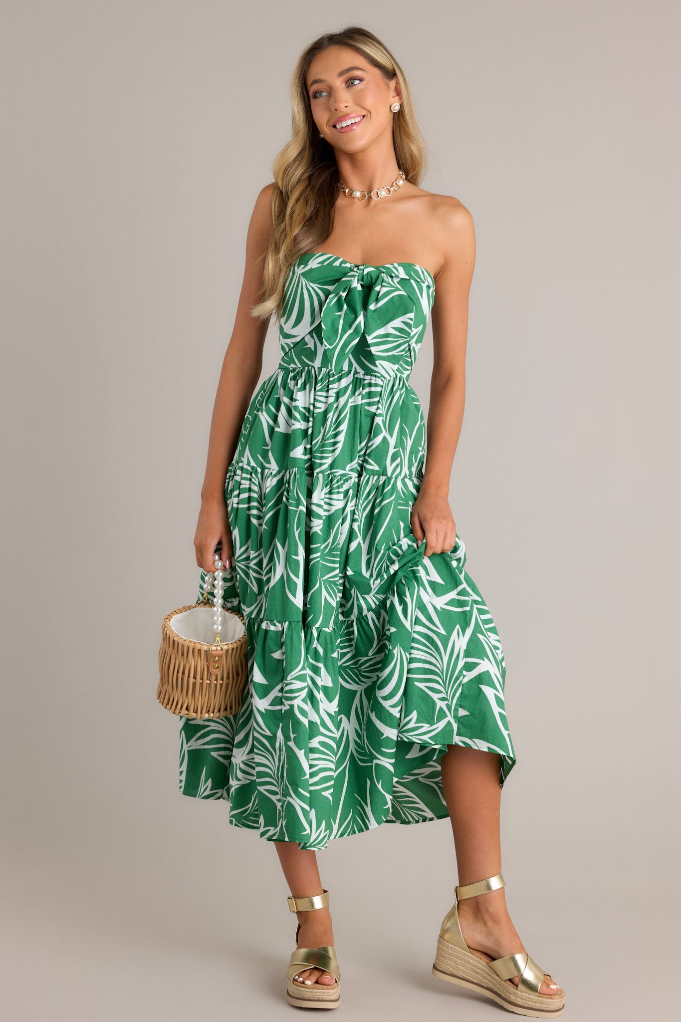 This green midi dress features a strapless neckline, boning in the bodice, a self-tie feature, a fully smocked insert in the back, and a tiered design.