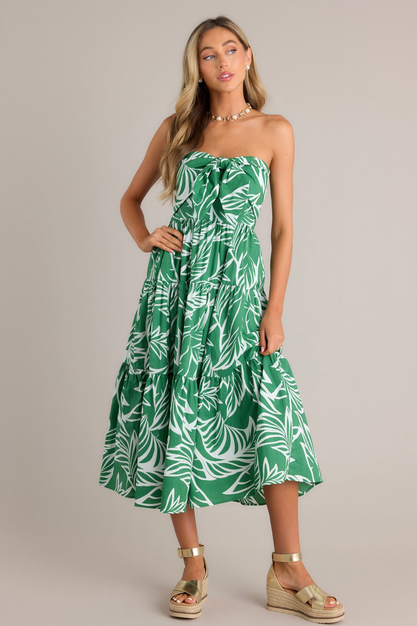 Front view of a green midi dress featuring a strapless neckline, boning in the bodice, a self-tie feature, a fully smocked insert in the back, and a tiered design.