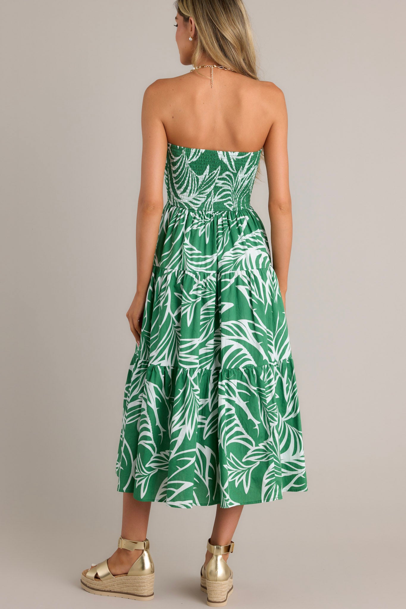 Back view of a green midi dress highlighting the fully smocked insert in the back, the strapless neckline, and the tiered design.