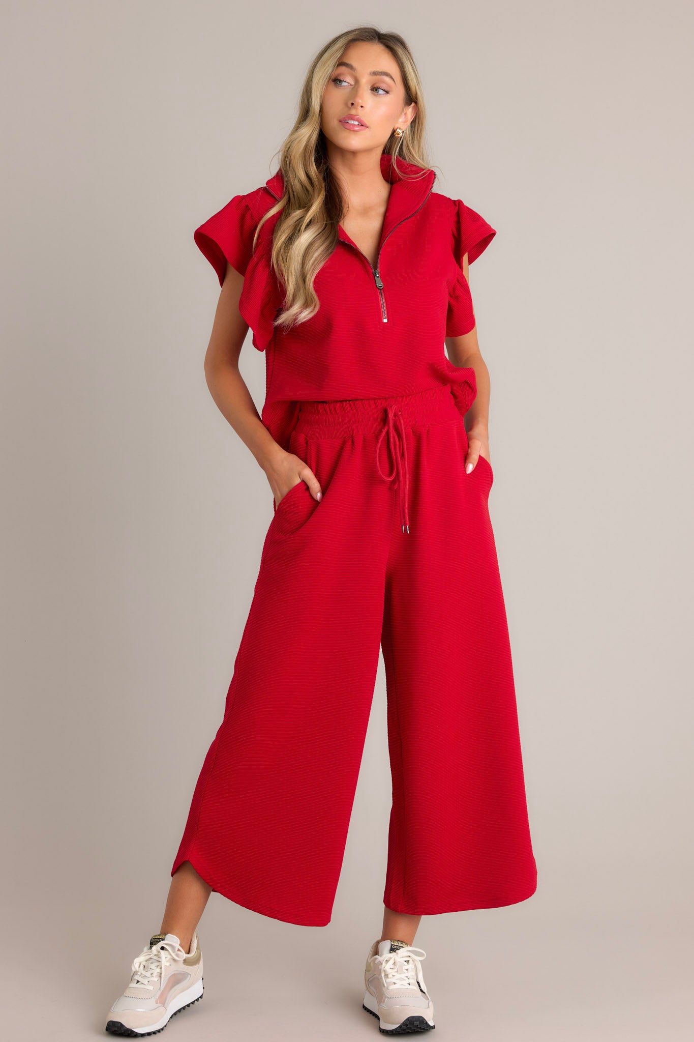 Full length view of red pants with a high waisted design, elastic waistband, self-tie drawstring, functional hip pockets, ribbed texture, wide leg, and scooped hemline
