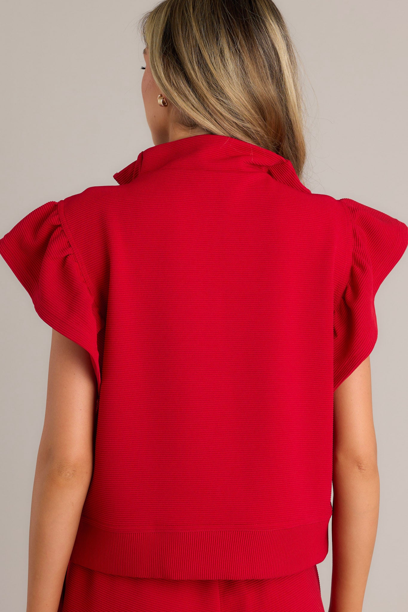 Back view of a red top highlighting the ribbed fabric, wide ruffled sleeves, and thick hemline.