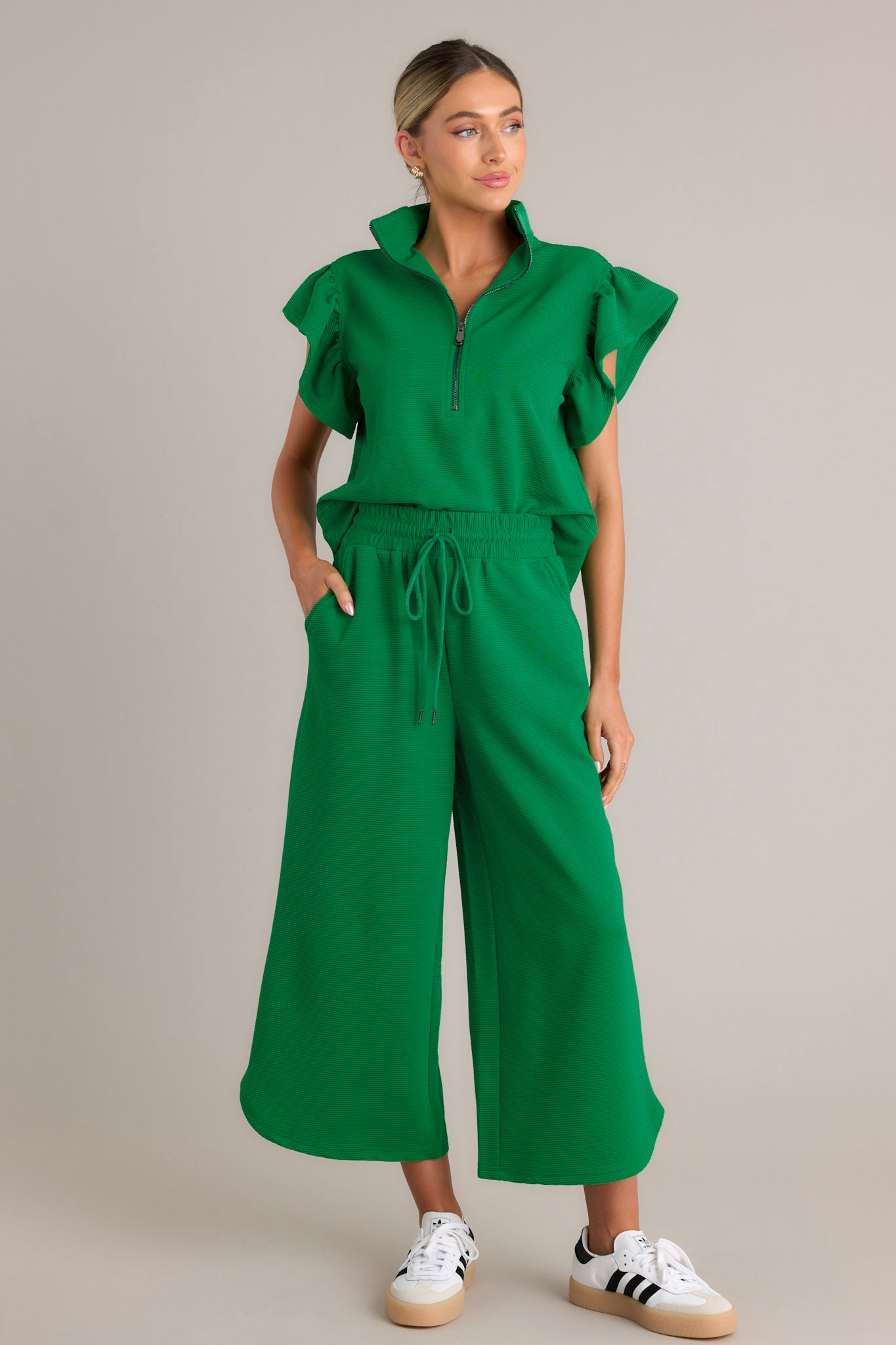 These green pants feature a high waisted design, an elastic waistband, a self-tie drawstring, functional hip pockets, a ribbed texture, a wide leg, and a scooped hemline.