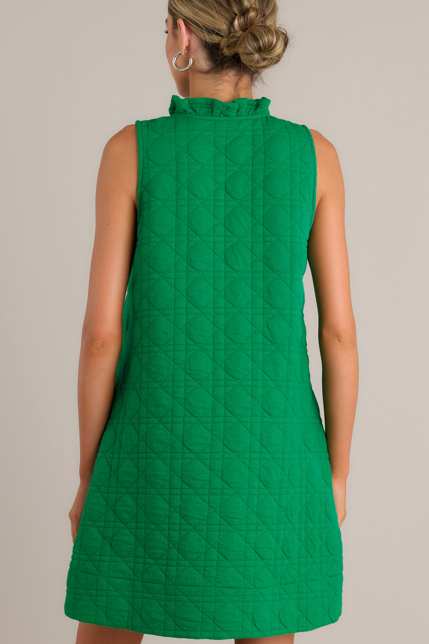 Back view of a green mini dress highlighting the unique quilted material and sleeveless design.