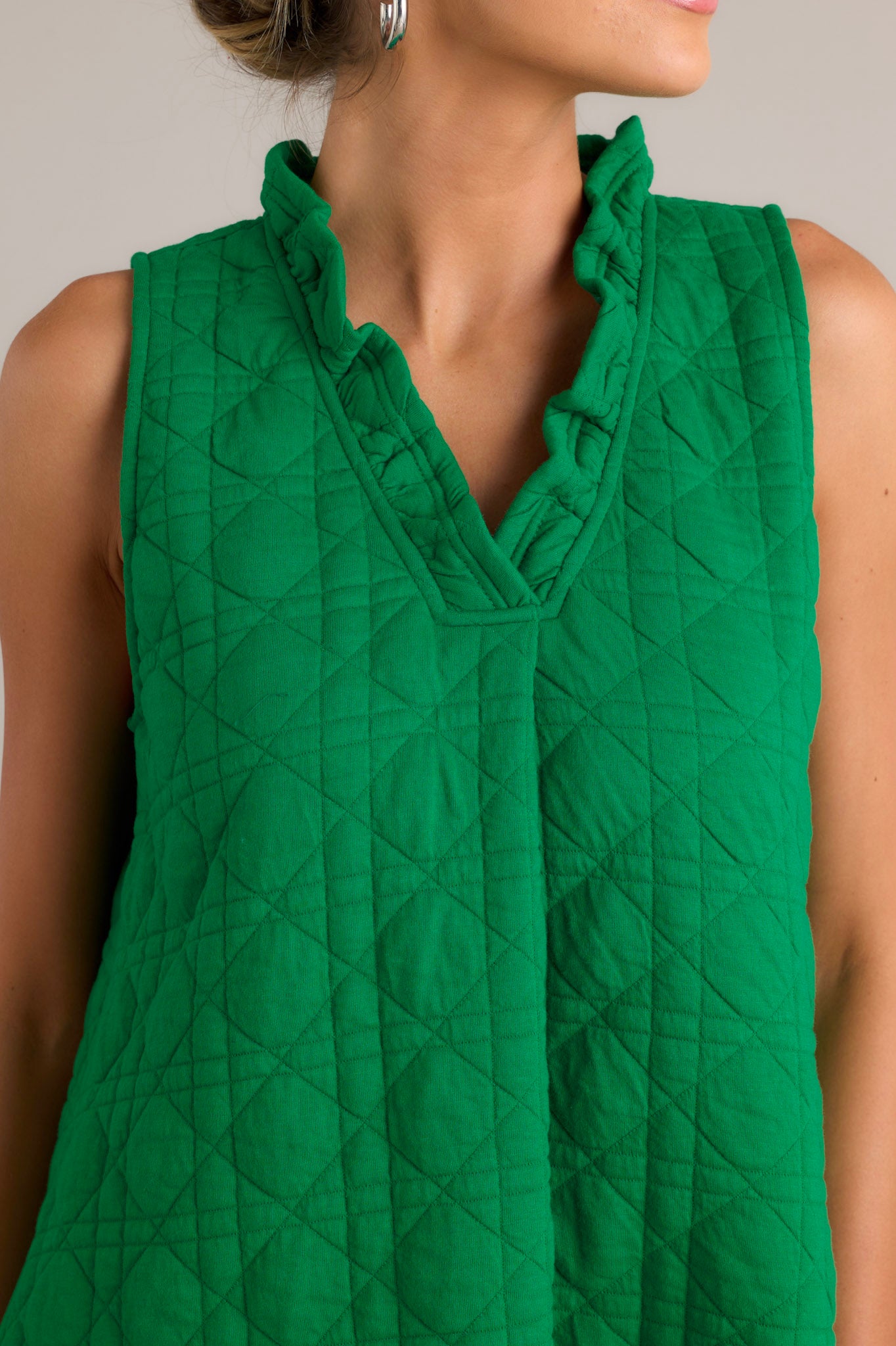 Close-up of the green mini dress showing the ruffled v-neckline, unique quilted material, and functional hip pockets.