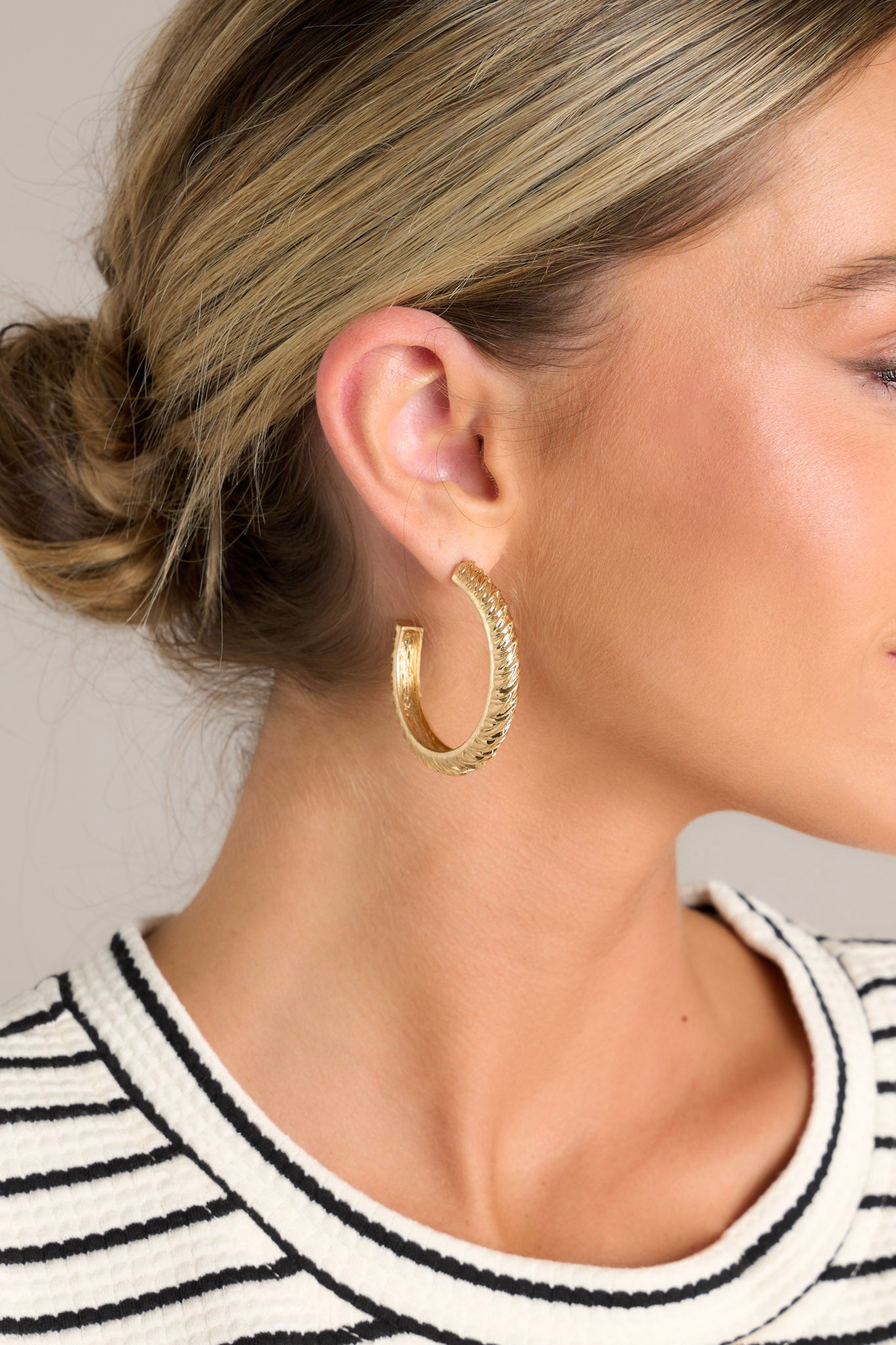Close up view of these gold hoop earrings that feature a gold finish, a grooved textured design, and secure post backings.