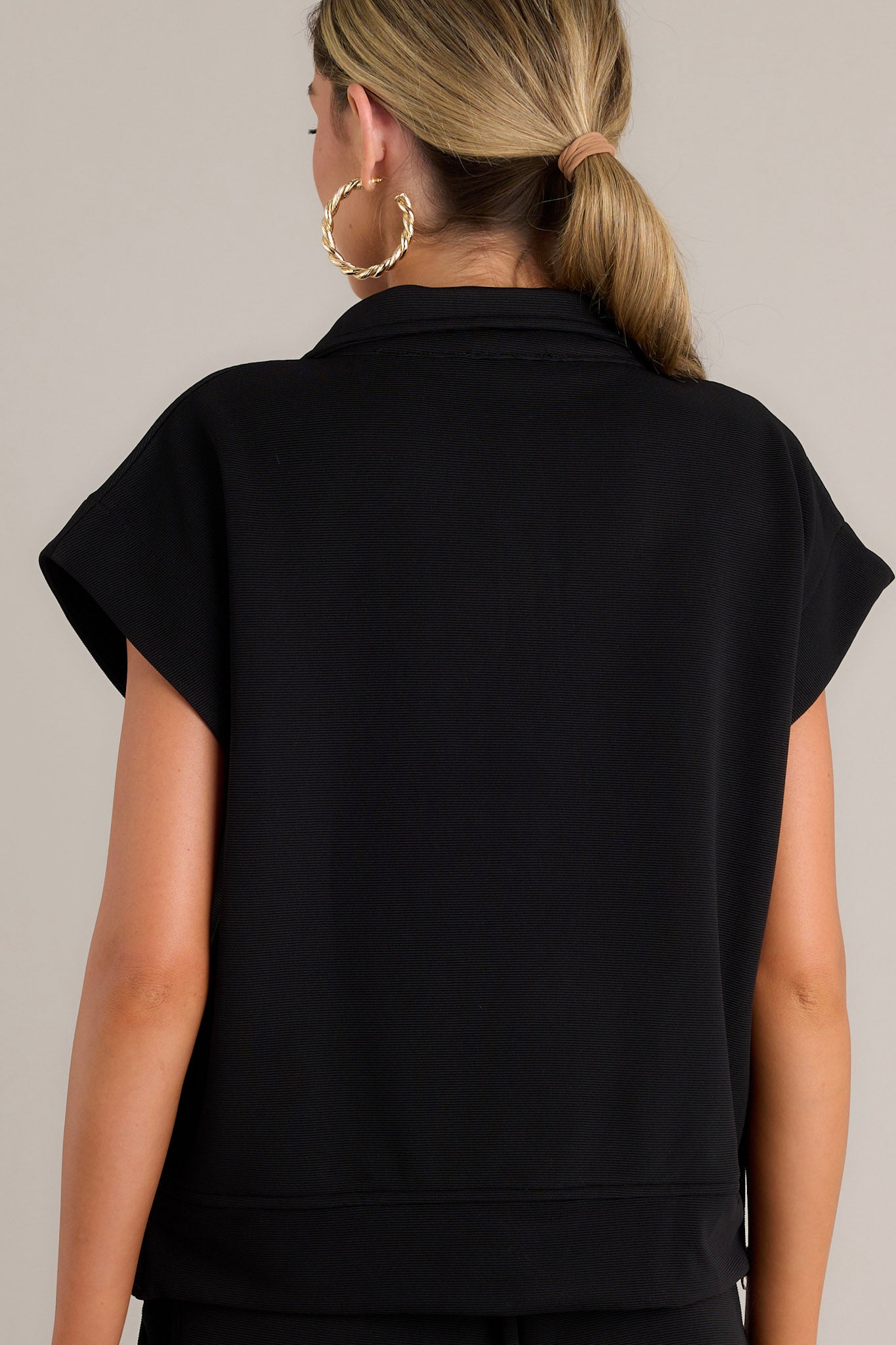 Back view of a black pullover highlighting the short cap sleeves and overall fit.
