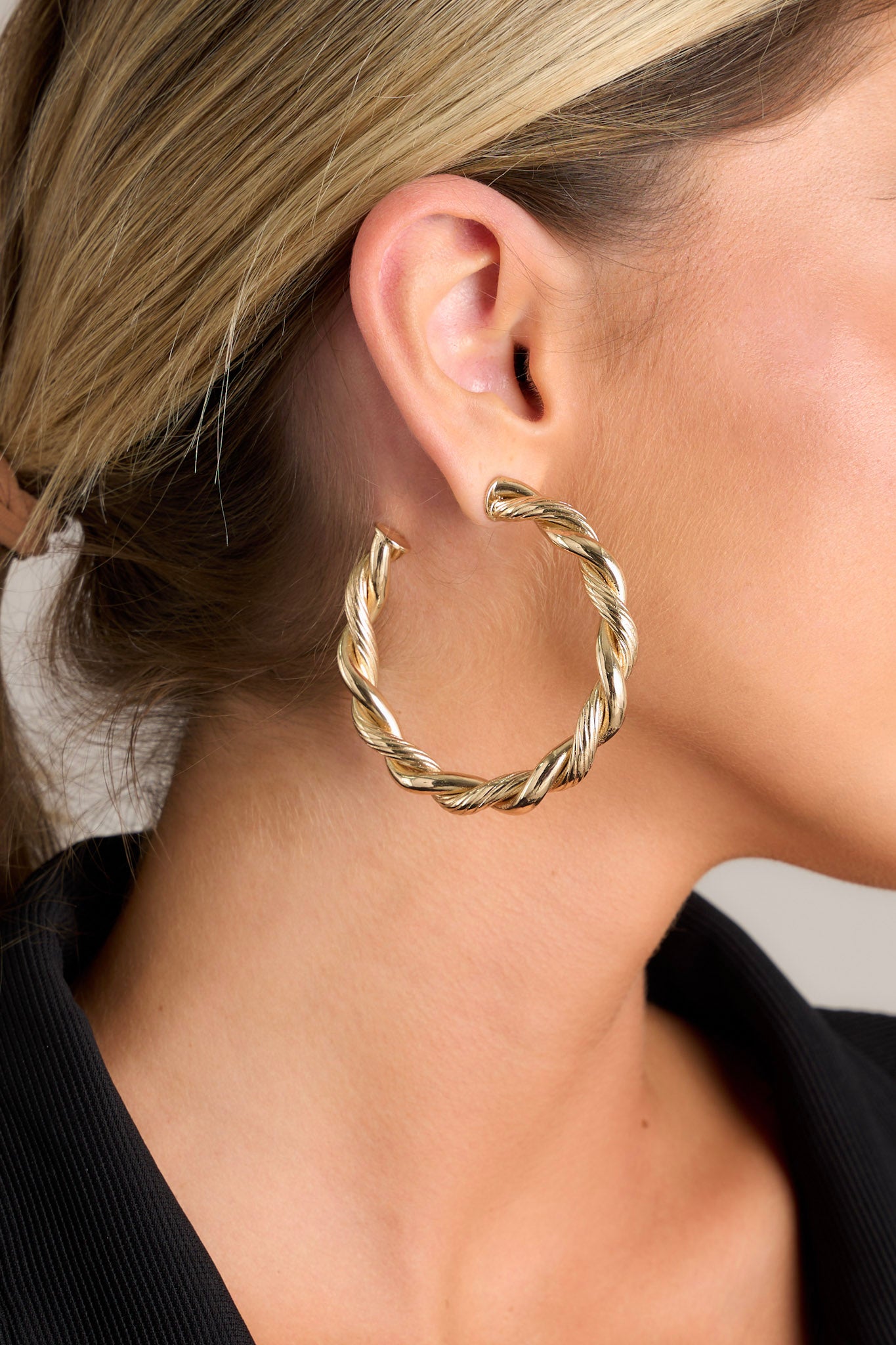 Close-up view of these gold earrings that feature an incomplete hoop design, a textured twisted design, and secure post backings.