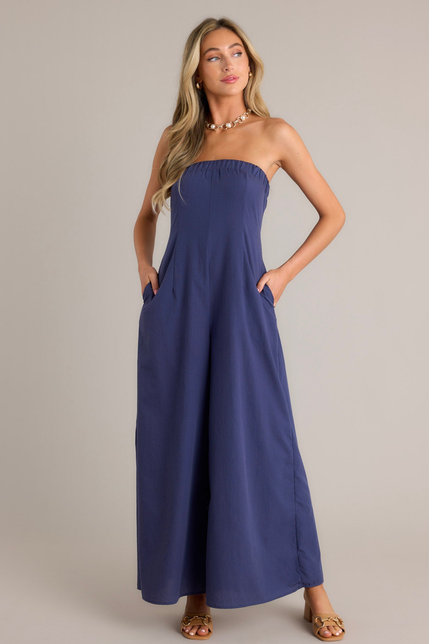 Front view of a navy jumpsuit featuring an elastic strapless neckline, a discrete side zipper, functional hip pockets, and a wide leg.