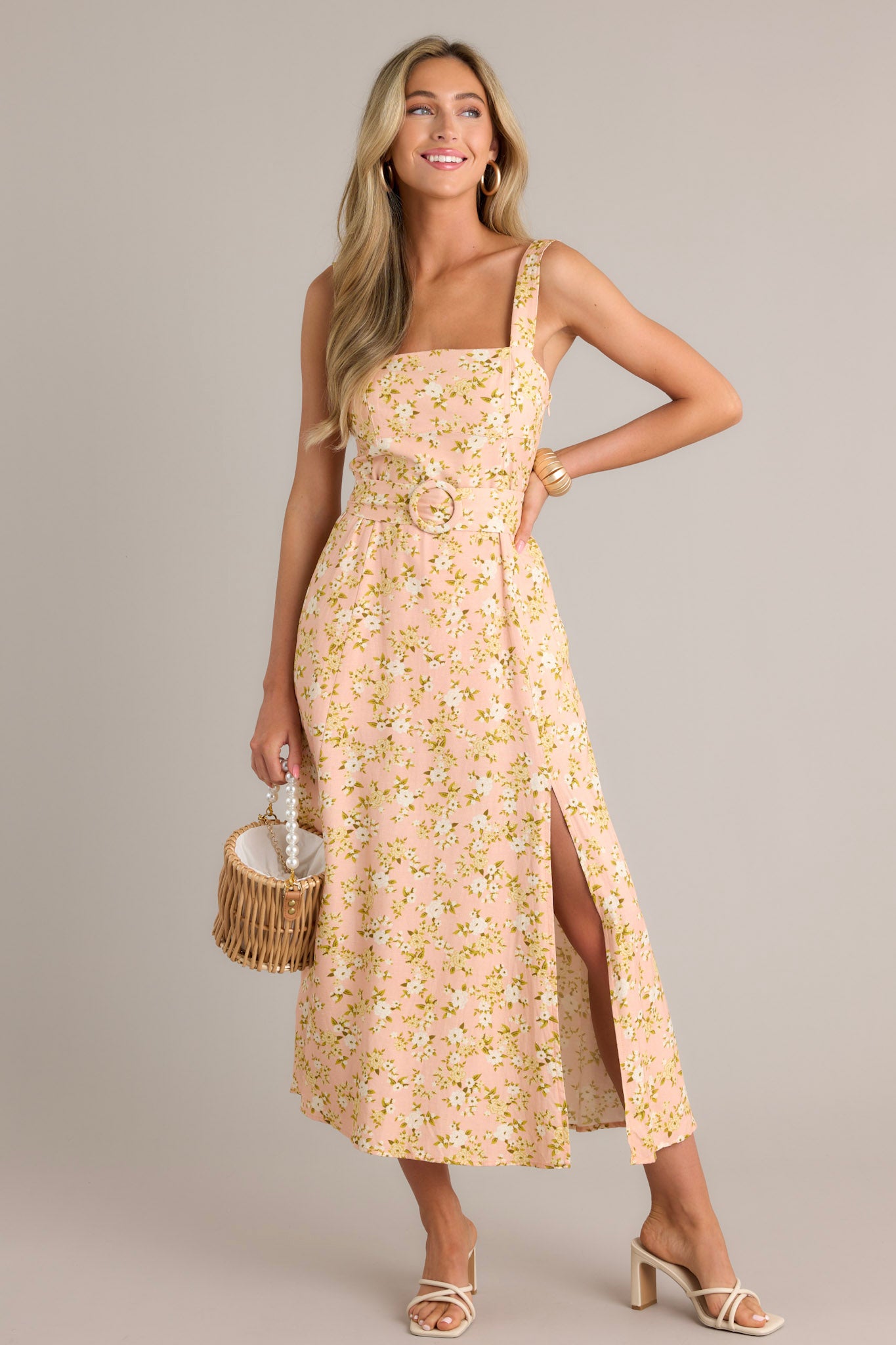 Front angled view of a peach maxi dress featuring a square neckline, thick adjustable straps, a smocked back insert, a discrete zipper, a functional pull-through waist belt, belt loops, functional hip pockets, and a front slit