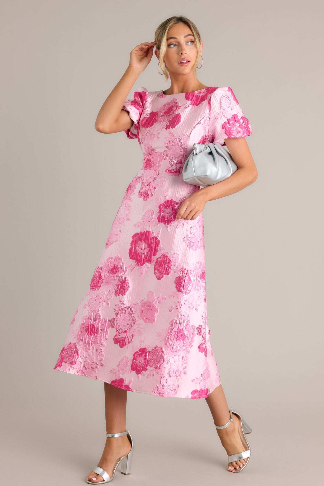 Action shot of a pink dress displaying the fit and movement, highlighting the boat neckline, short puff sleeves, deep v-back with a zipper closure, and midi length.
