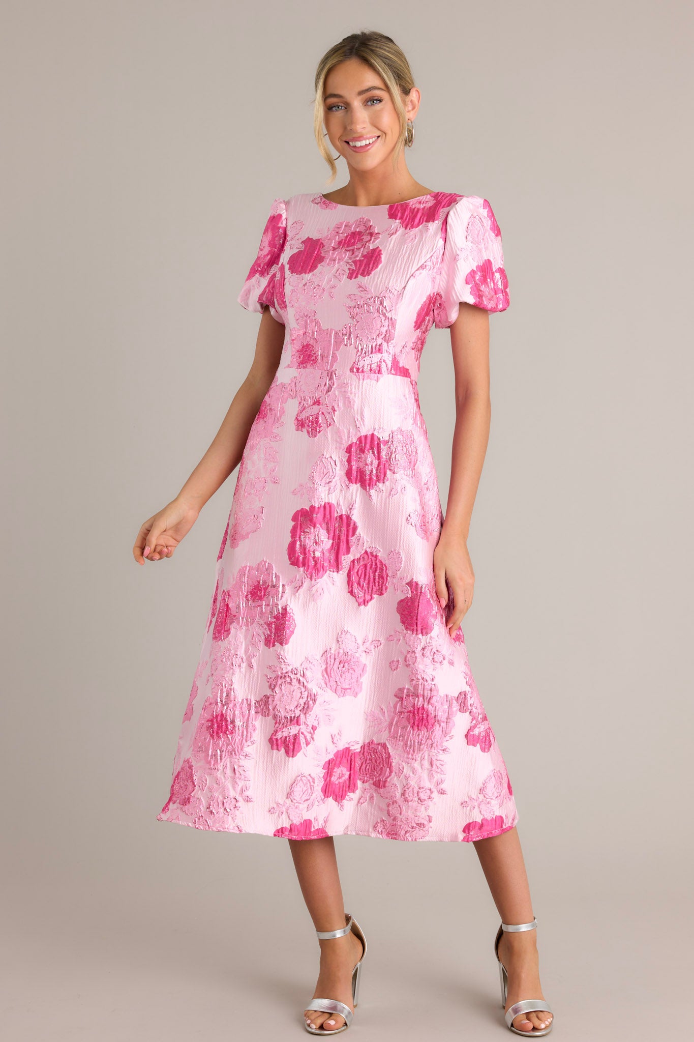 Front angled view of a pink dress featuring a boat neckline, short puff sleeves, a deep v-back with a zipper closure, and a midi length