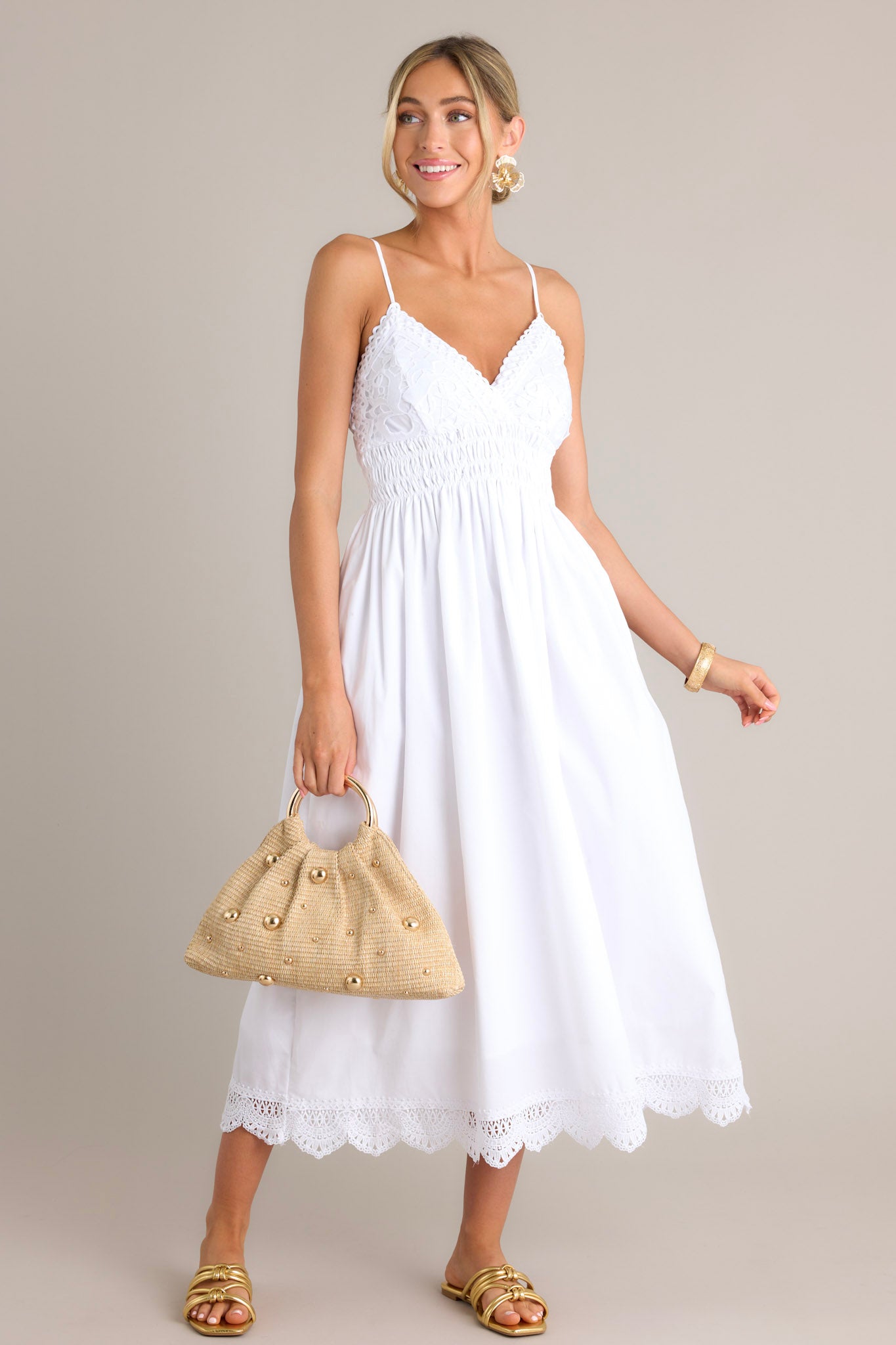 Full length view of a white maxi dress with a v-neckline, thin adjustable straps, a lace bust, a fully smocked waist & back, a flowing silhouette, and a lace hemline