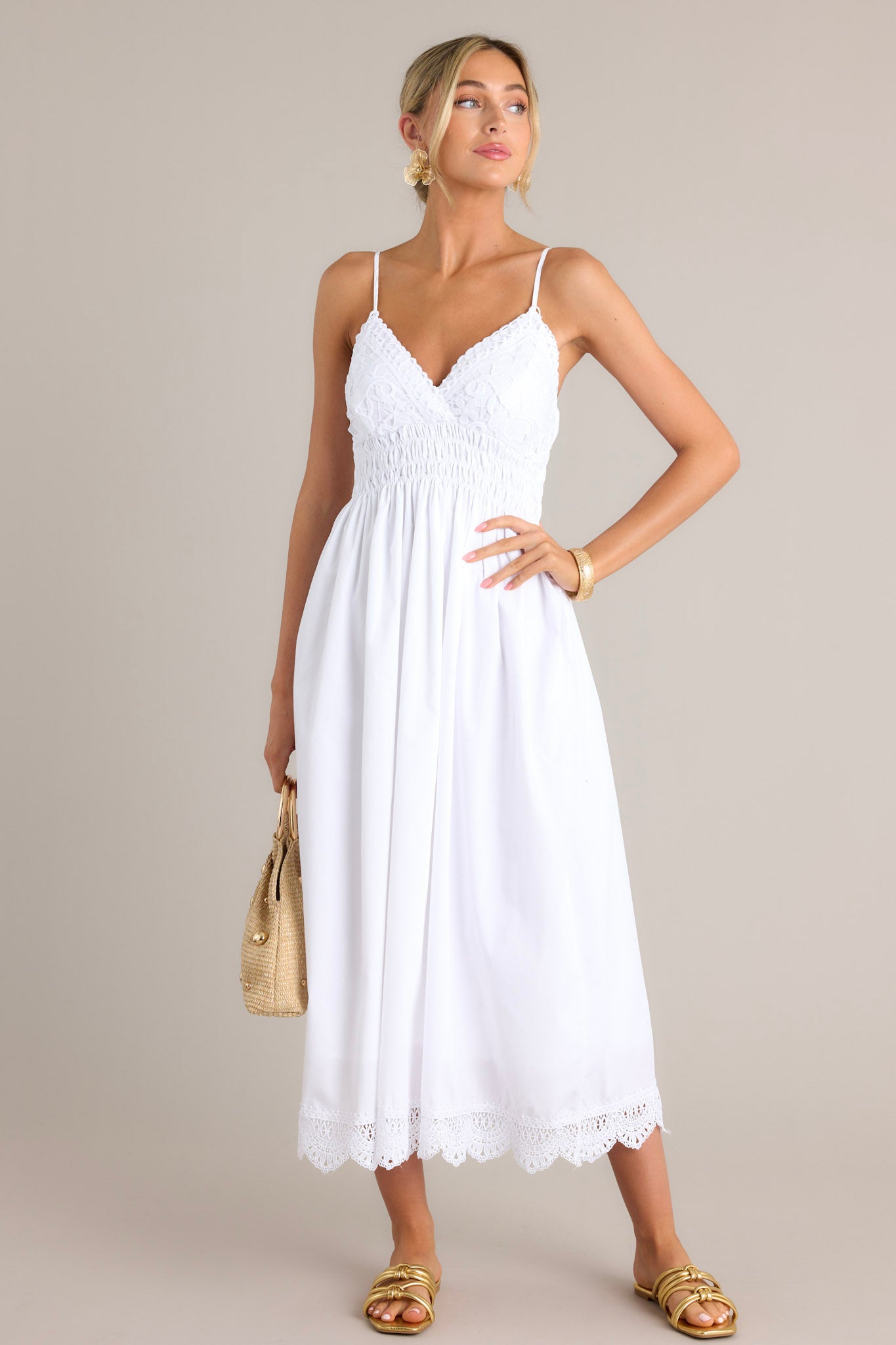 This white maxi dress features a v-neckline, thin adjustable straps, a lace bust, a fully smocked waist back, a flowing silhouette, and a lace hemline.