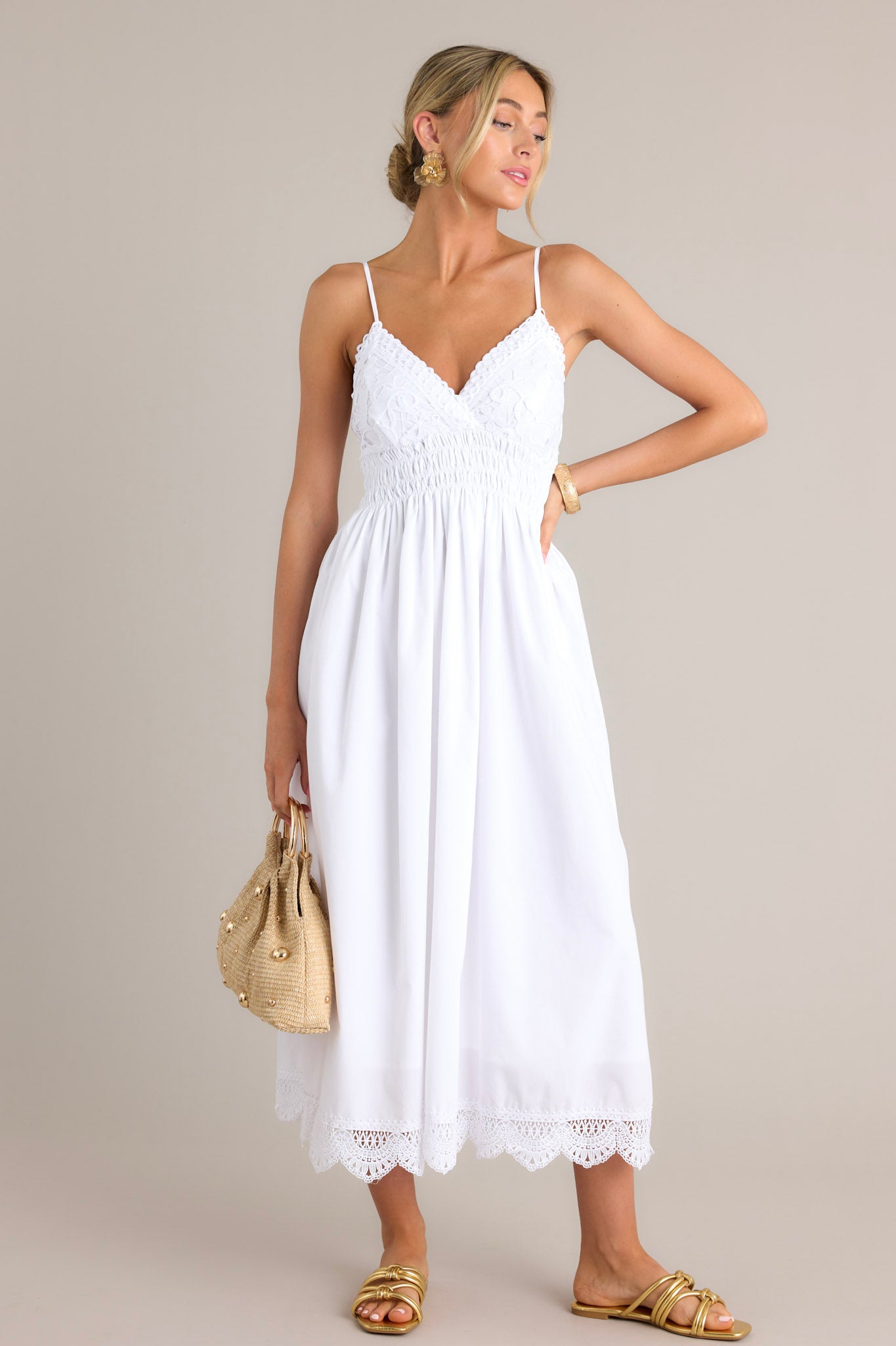 Front angled view of a white maxi dress featuring a v-neckline, thin adjustable straps, a lace bust, a fully smocked waist & back, a flowing silhouette, and a lace hemline