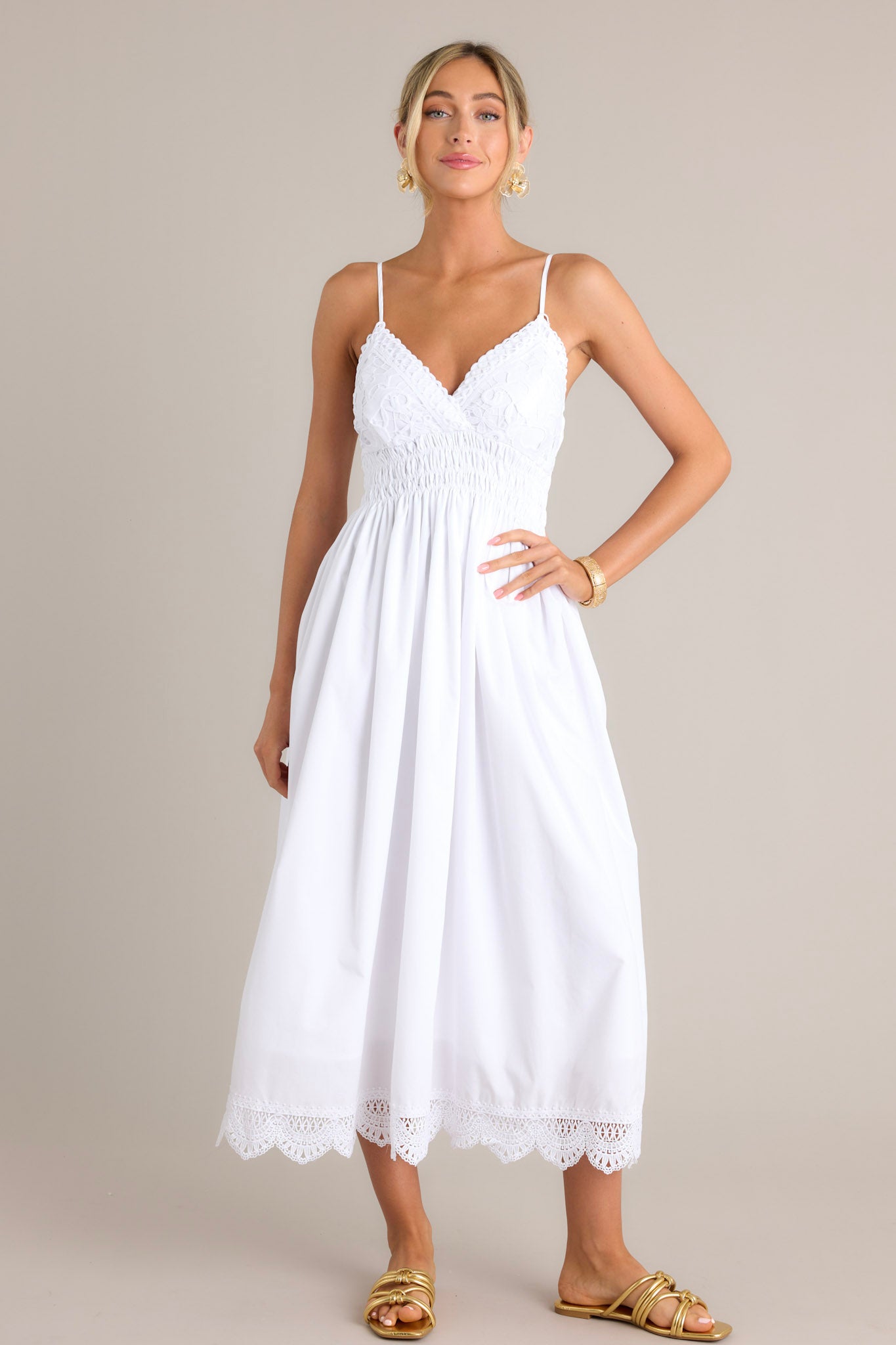 Front view of a white maxi dress featuring a v-neckline, thin adjustable straps, a lace bust, a fully smocked waist & back, a flowing silhouette, and a lace hemline.