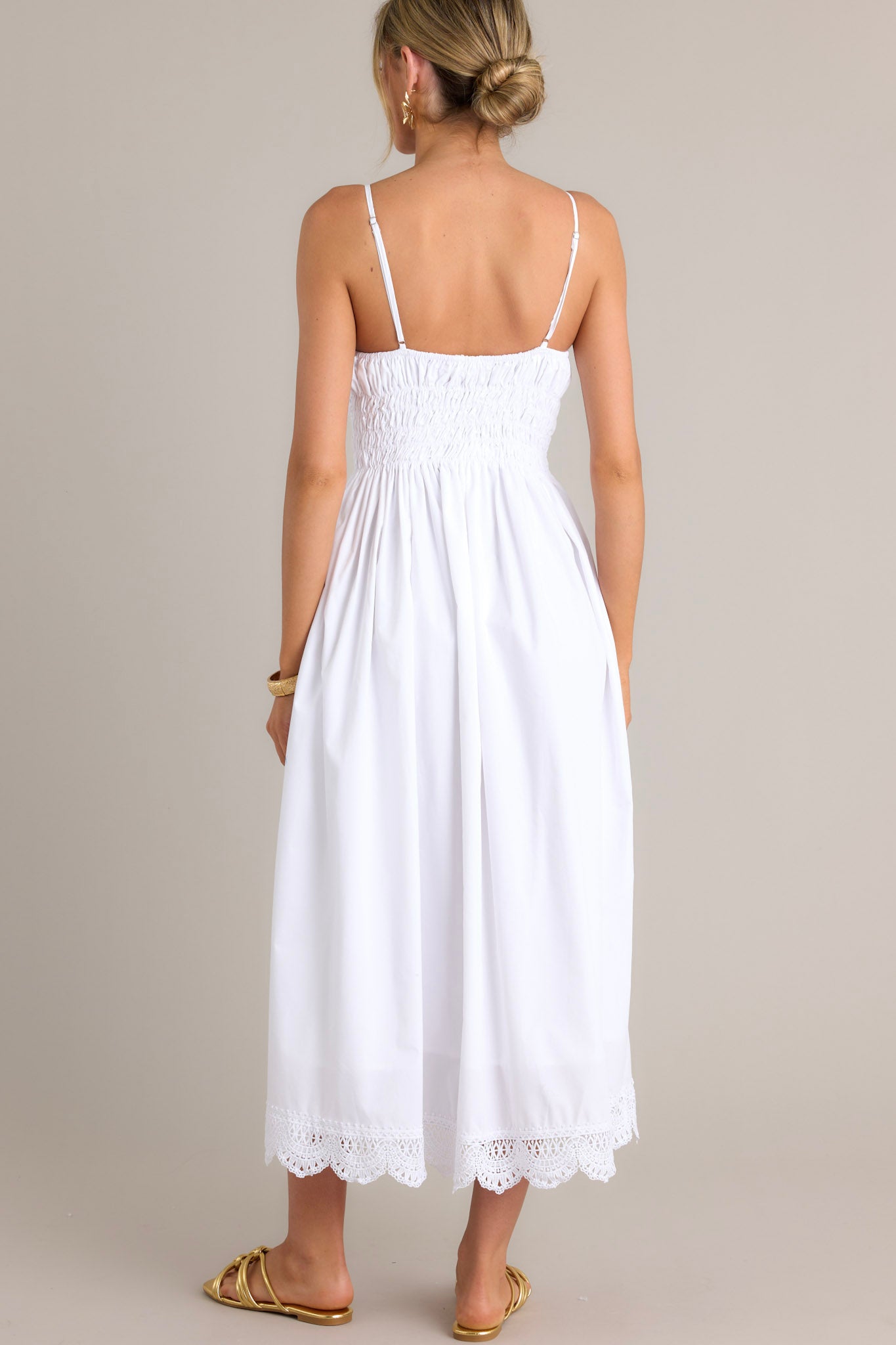 Back view of a white maxi dress highlighting the thin adjustable straps, fully smocked back, and lace hemline.