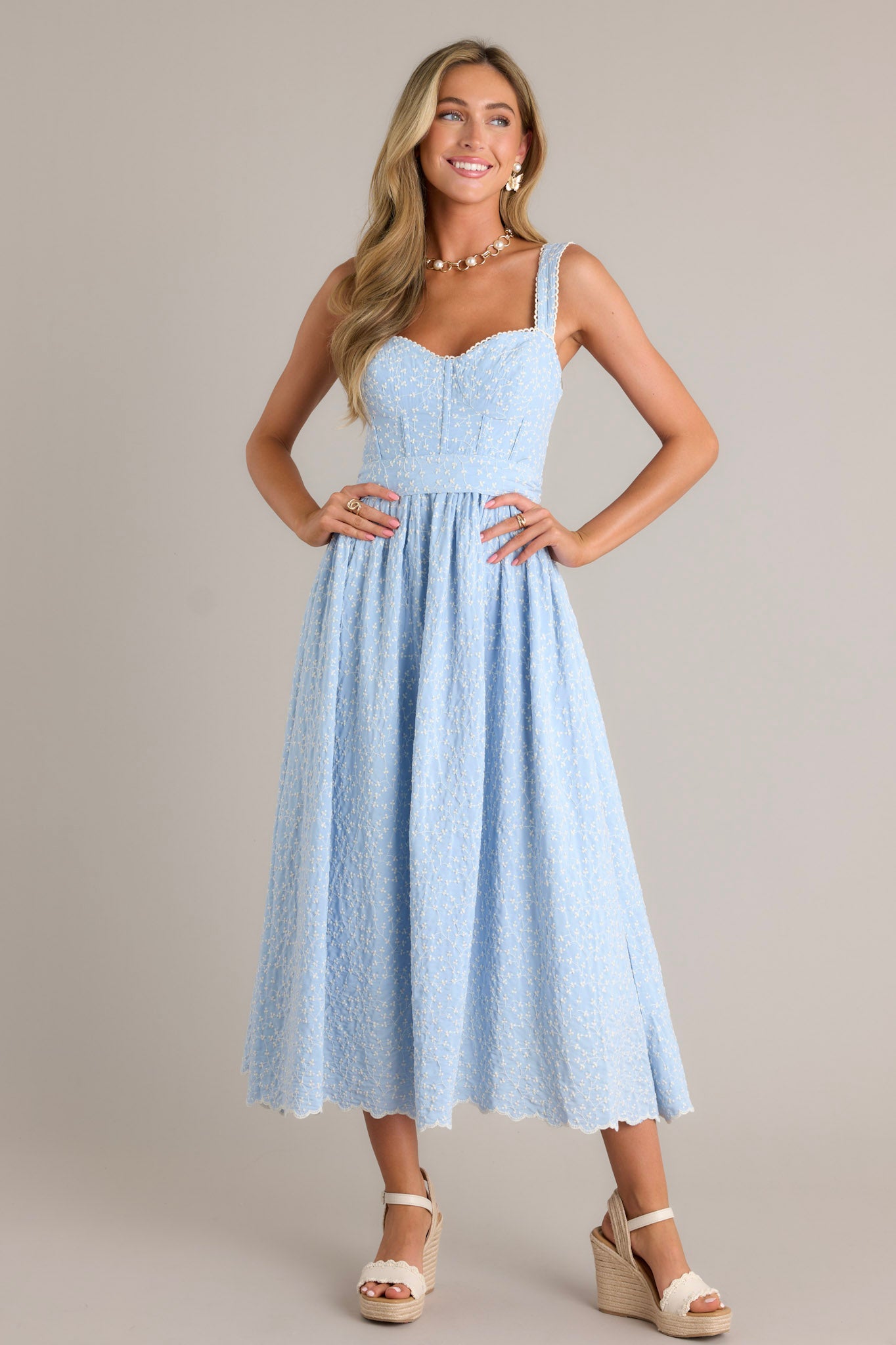 This light blue midi dress features a sweetheart neckline, a smocked back insert, a zipper, thick adjustable straps, boning in the bodice, a self-tie waist belt, and embroidery throughout.