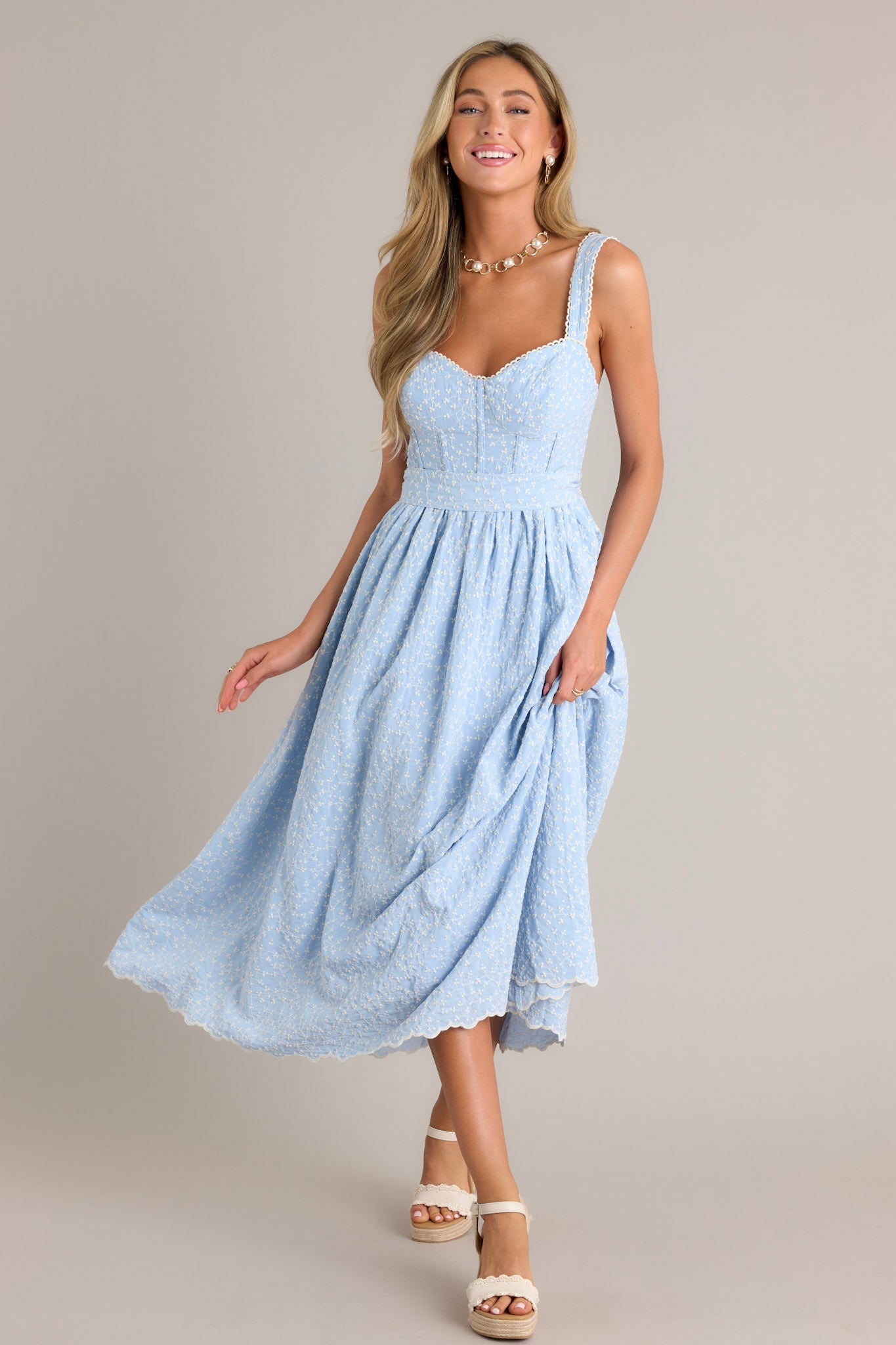 Action shot of a light blue midi dress displaying the fit and movement, highlighting the sweetheart neckline, smocked back insert, thick adjustable straps, boning in the bodice, self-tie waist belt, and embroidery.