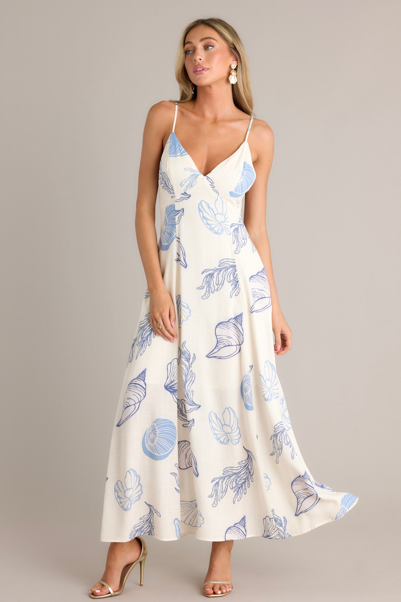 Front view of a blue maxi dress featuring a v-neckline, thin adjustable straps with a self-tie feature, functional hip pockets, a flowing silhouette, and a tropical print.