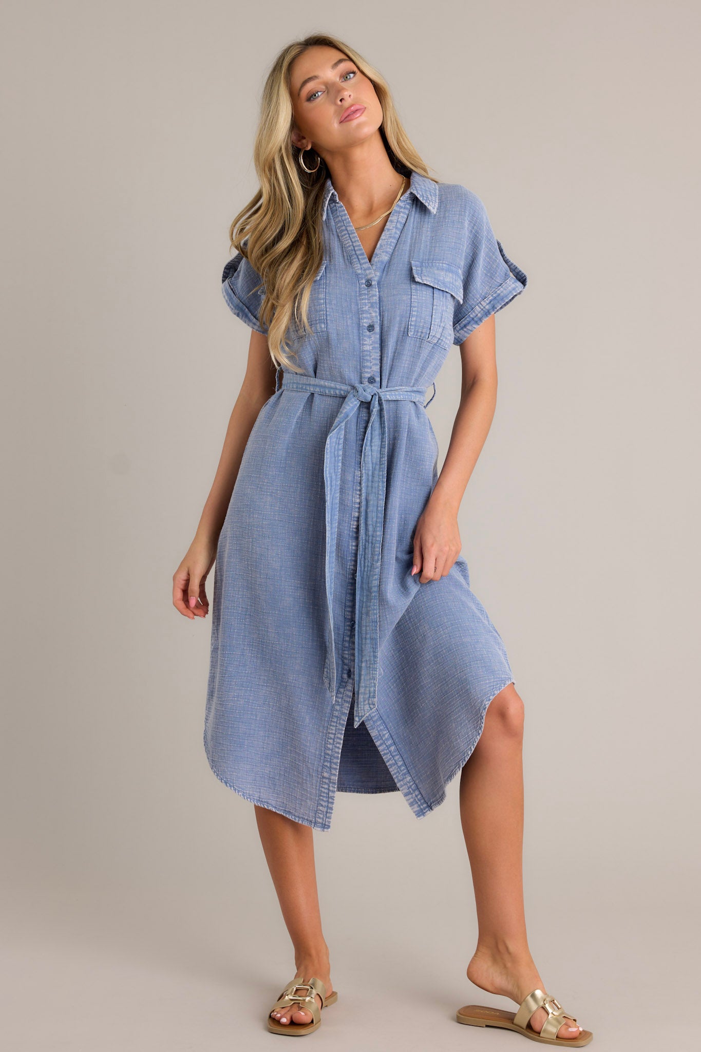 Full length view of a blue maxi dress with a collared v-neckline, a functional button front, functional breast pockets, a self-tie waist belt, belt loops, and cuffed short sleeves