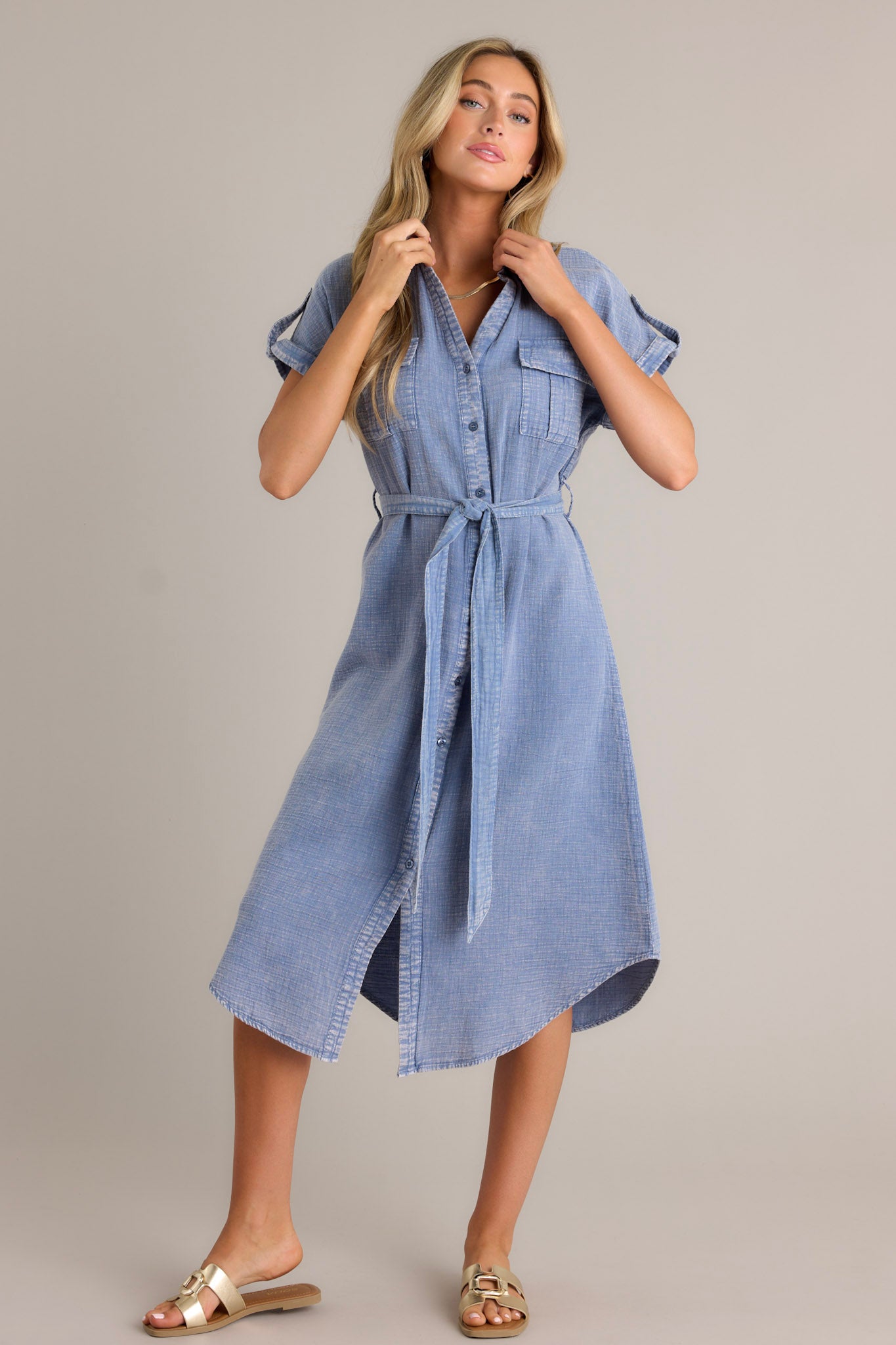 Front view of a blue maxi dress featuring a collared v-neckline, a functional button front, functional breast pockets, a self-tie waist belt, belt loops, and cuffed short sleeves.