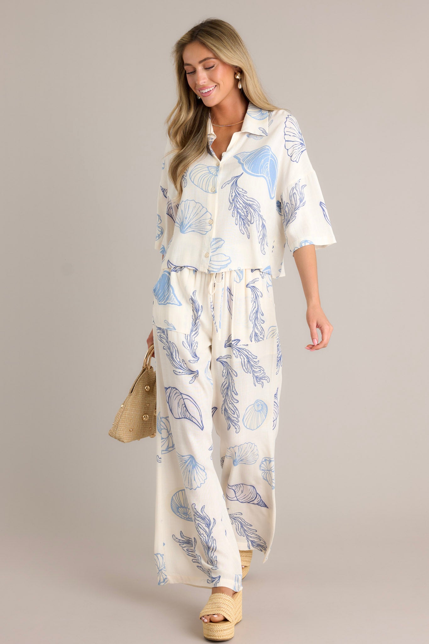 Full length view of a top with a collared neckline, a full button front, a seashell print on lightweight fabric, and a slightly cropped length