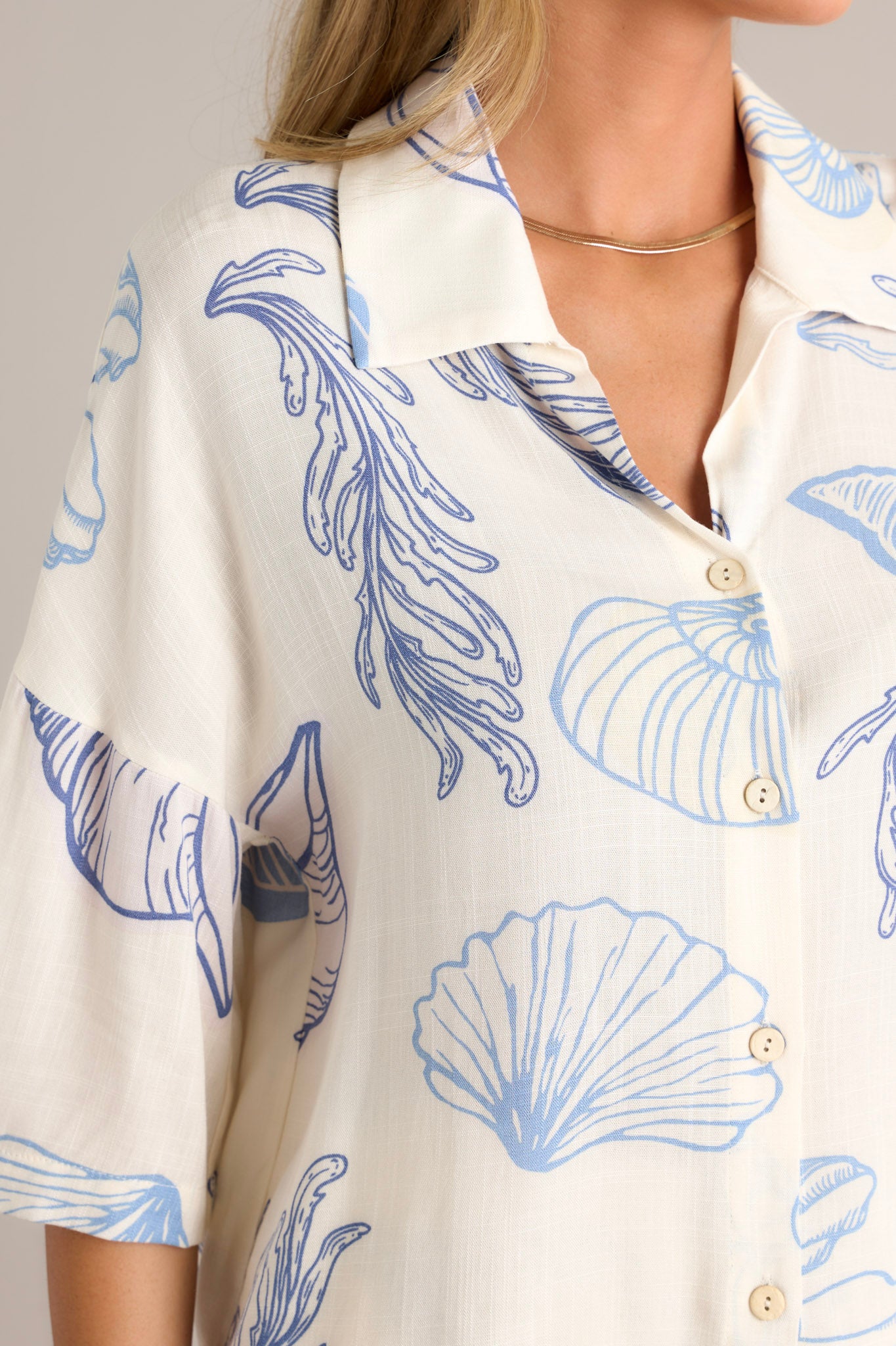 Close-up of the top showing the collared neckline, full button front, and the seashell print on lightweight fabric.