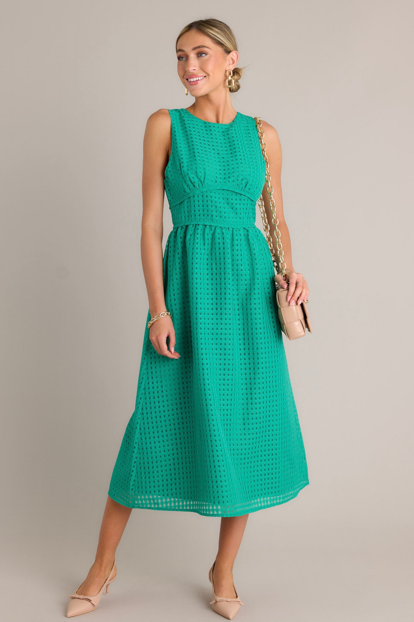 Front angled view of a green midi dress featuring a high neckline, a discrete back zipper, a thick waistband, a grid-like pattern, and a sleeveless design