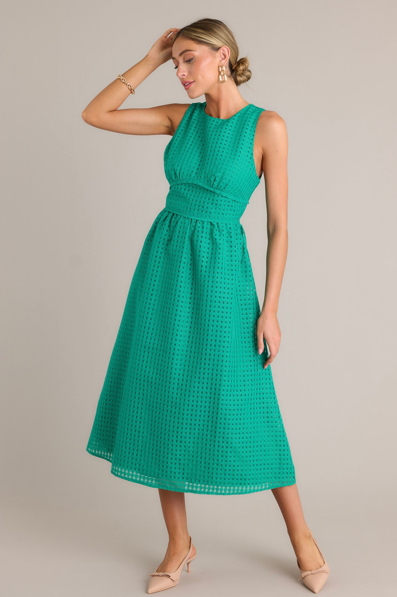 Action shot of a green midi dress displaying the fit and movement, highlighting the high neckline, thick waistband, grid-like pattern, and sleeveless design.