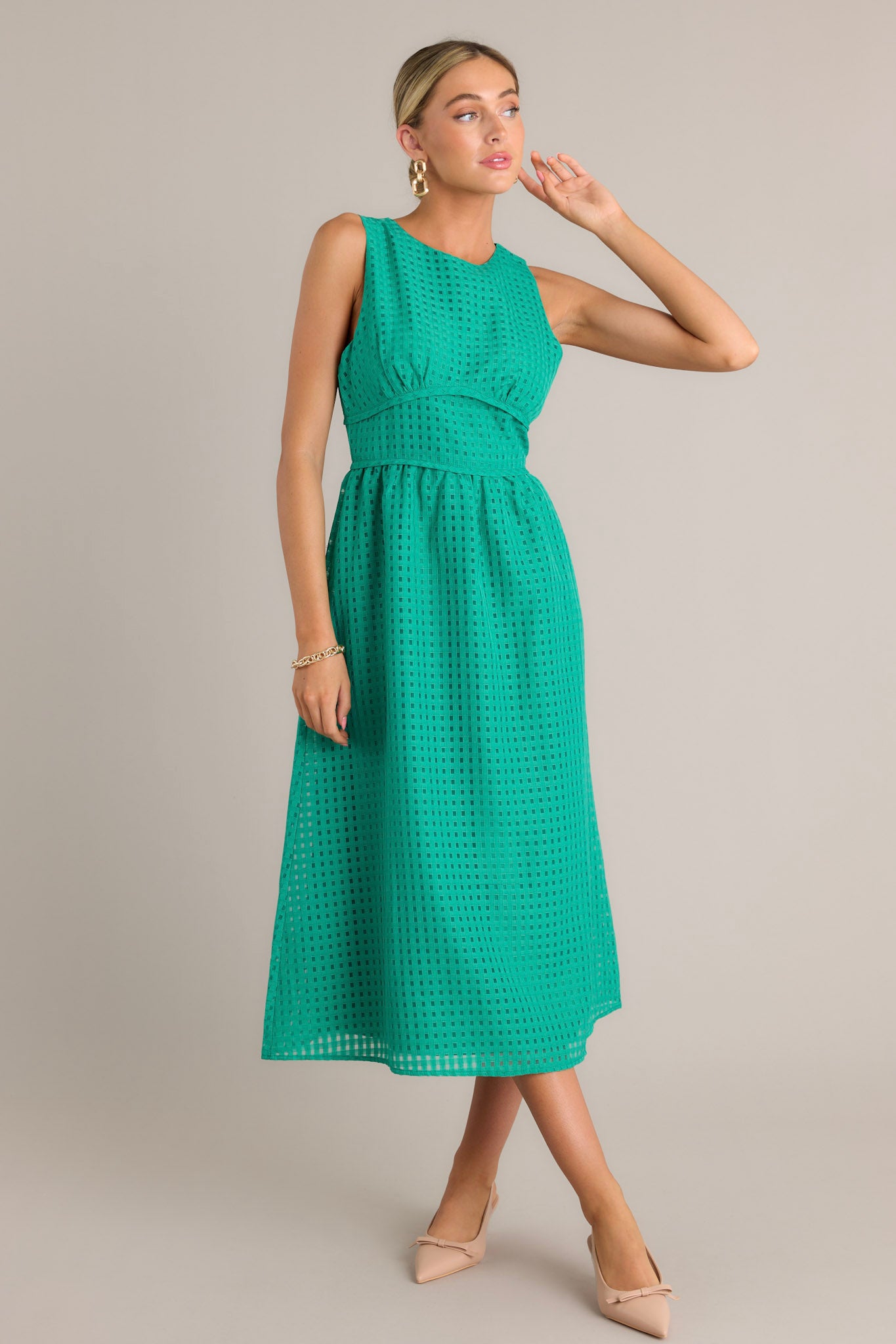 Full length view of a green midi dress with a high neckline, a discrete back zipper, a thick waistband, a grid-like pattern, and a sleeveless design