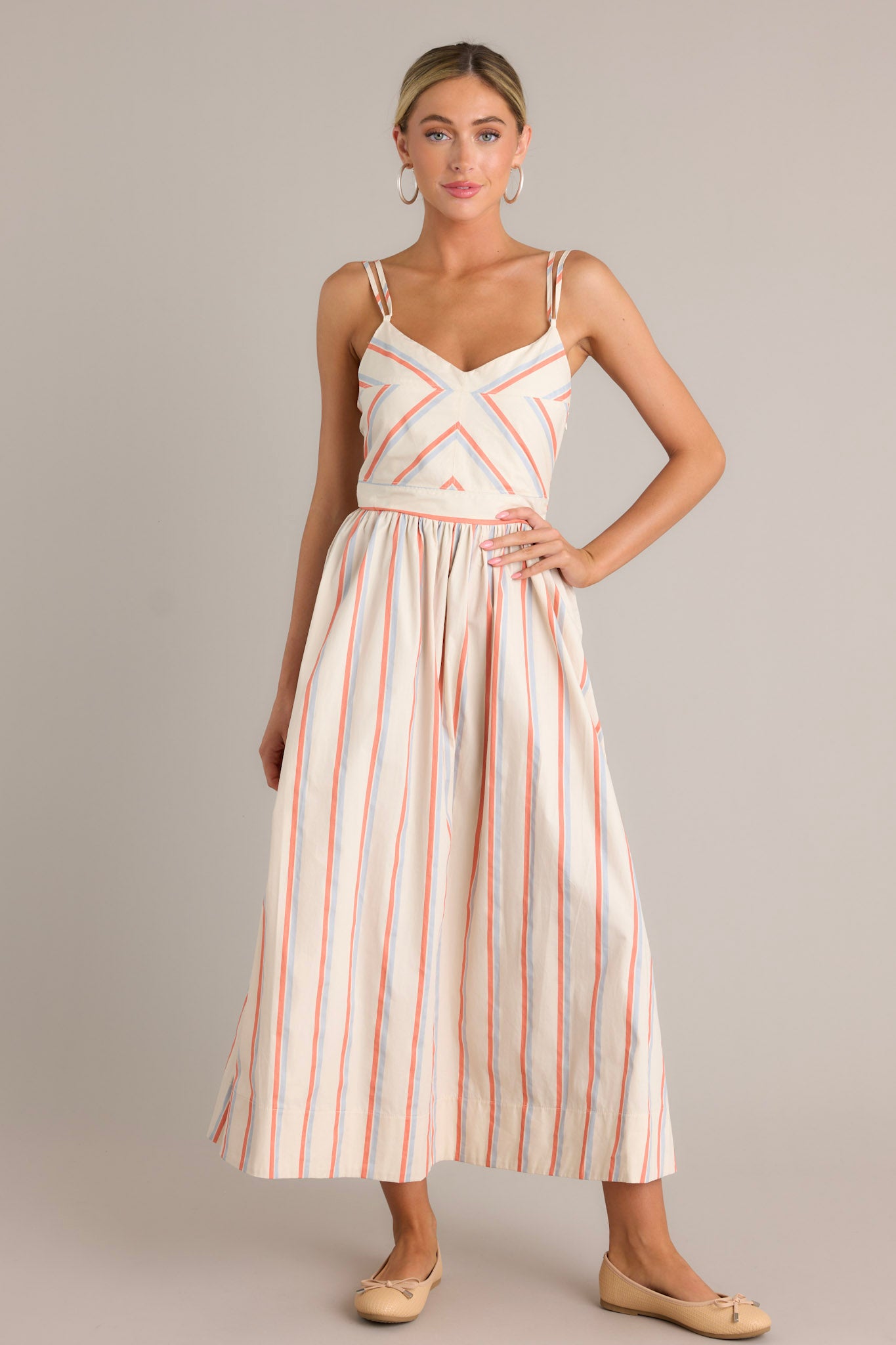 Front view of a multi stripe dress featuring a v-neckline, thin adjustable double straps, a smocked back insert, a discrete side zipper, a flowing silhouette, and a thick hemline.