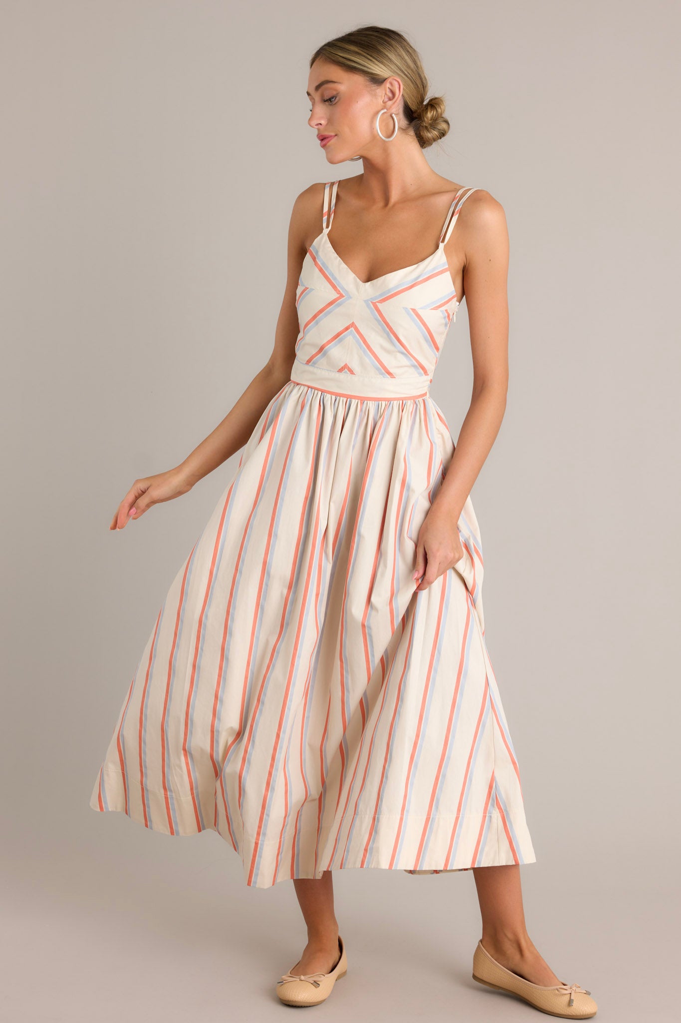 Front angled view of a multi stripe dress featuring a v-neckline, thin adjustable double straps, a smocked back insert, a discrete side zipper, a flowing silhouette, and a thick hemline