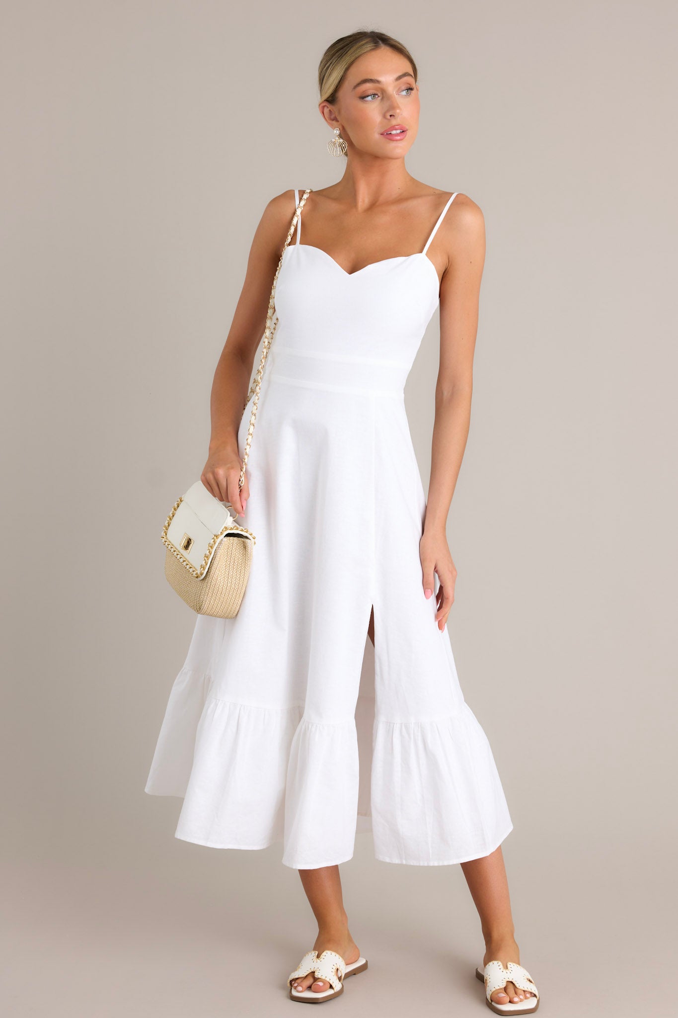 Full length view of a white maxi dress with a sweetheart neckline, thin adjustable straps, a smocked back insert, a discrete zipper, a single tier, and a slit