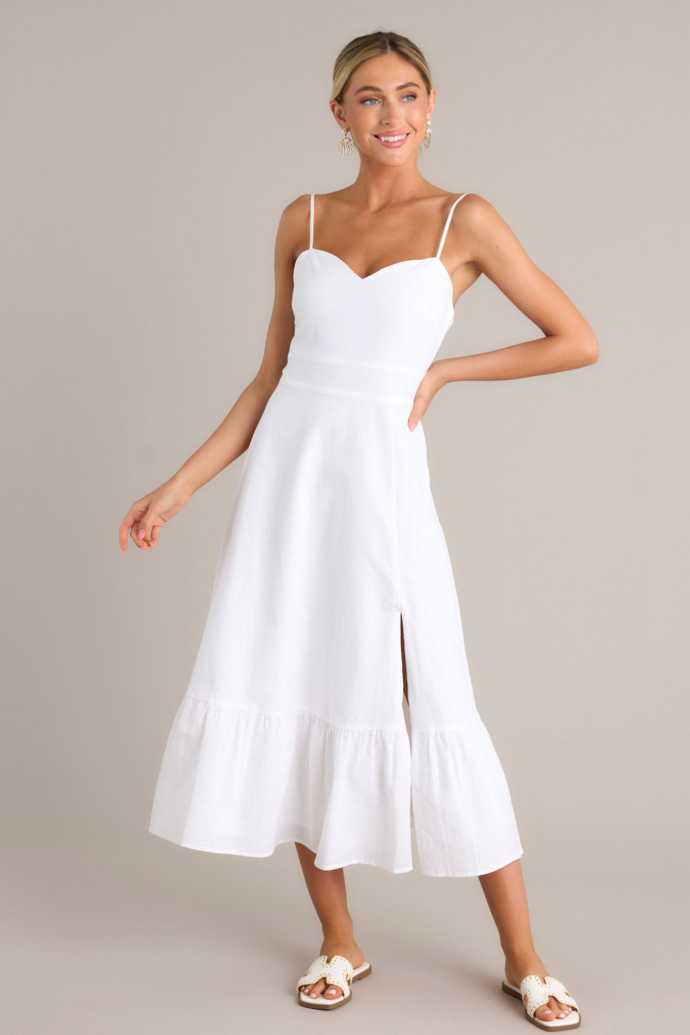 Action shot of a white maxi dress displaying the fit and movement, highlighting the sweetheart neckline, thin adjustable straps, smocked back insert, single tier, and slit.
