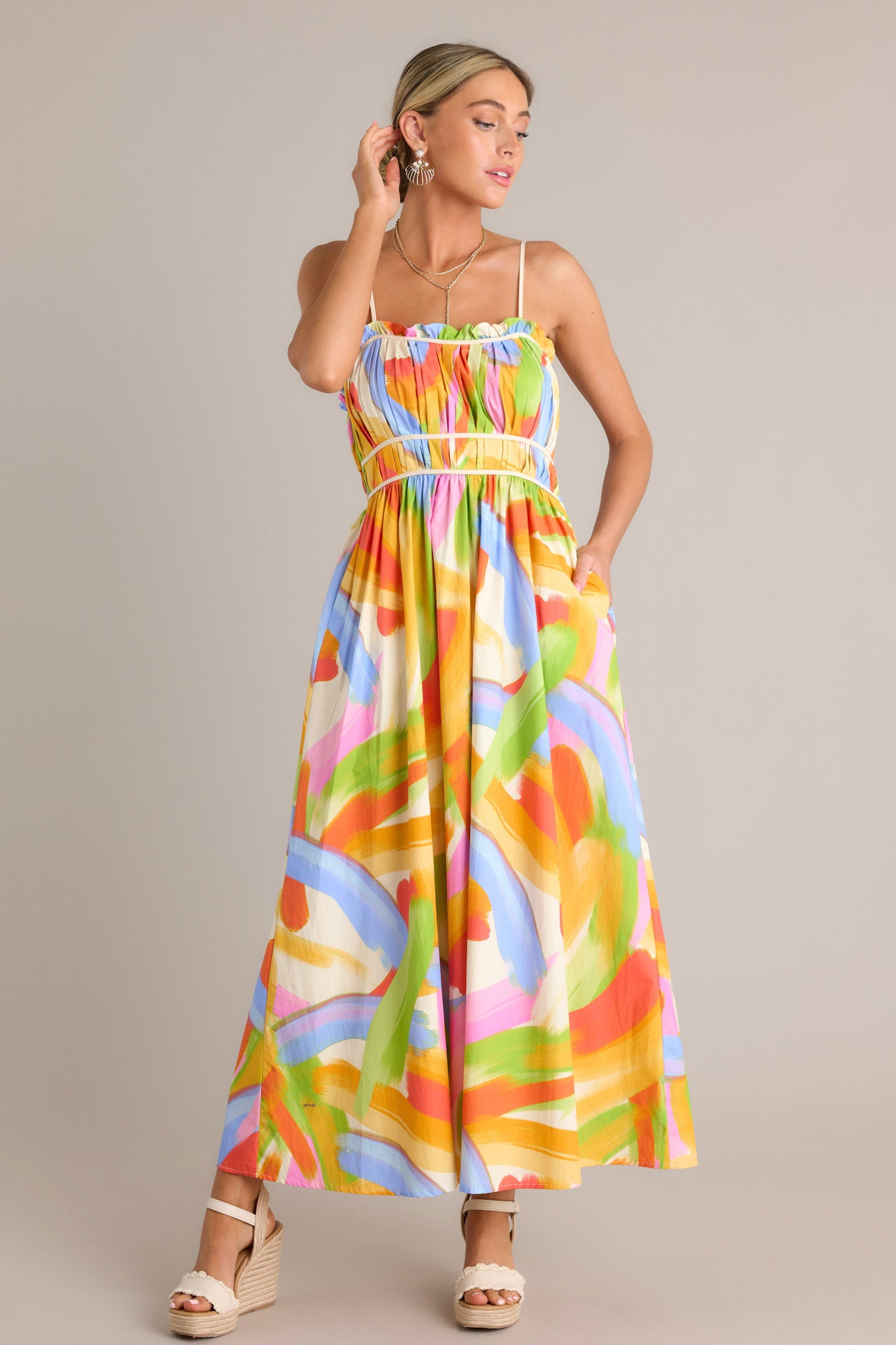 Full length view of a yellow multi maxi dress with a square neckline, thin adjustable straps, a pleated chest, elastic waist inserts, functional hip pockets, and a flowing silhouette