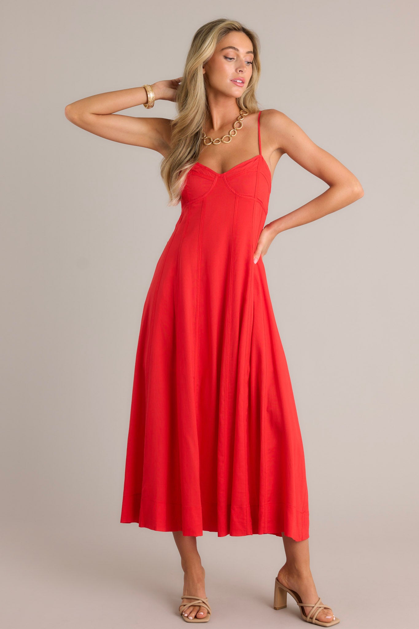 Front angled view of a red maxi dress featuring a sweetheart neckline, thin adjustable straps, no boning in the bodice for a bustier look, a smocked back insert, a discrete zipper, and a flowing silhouette