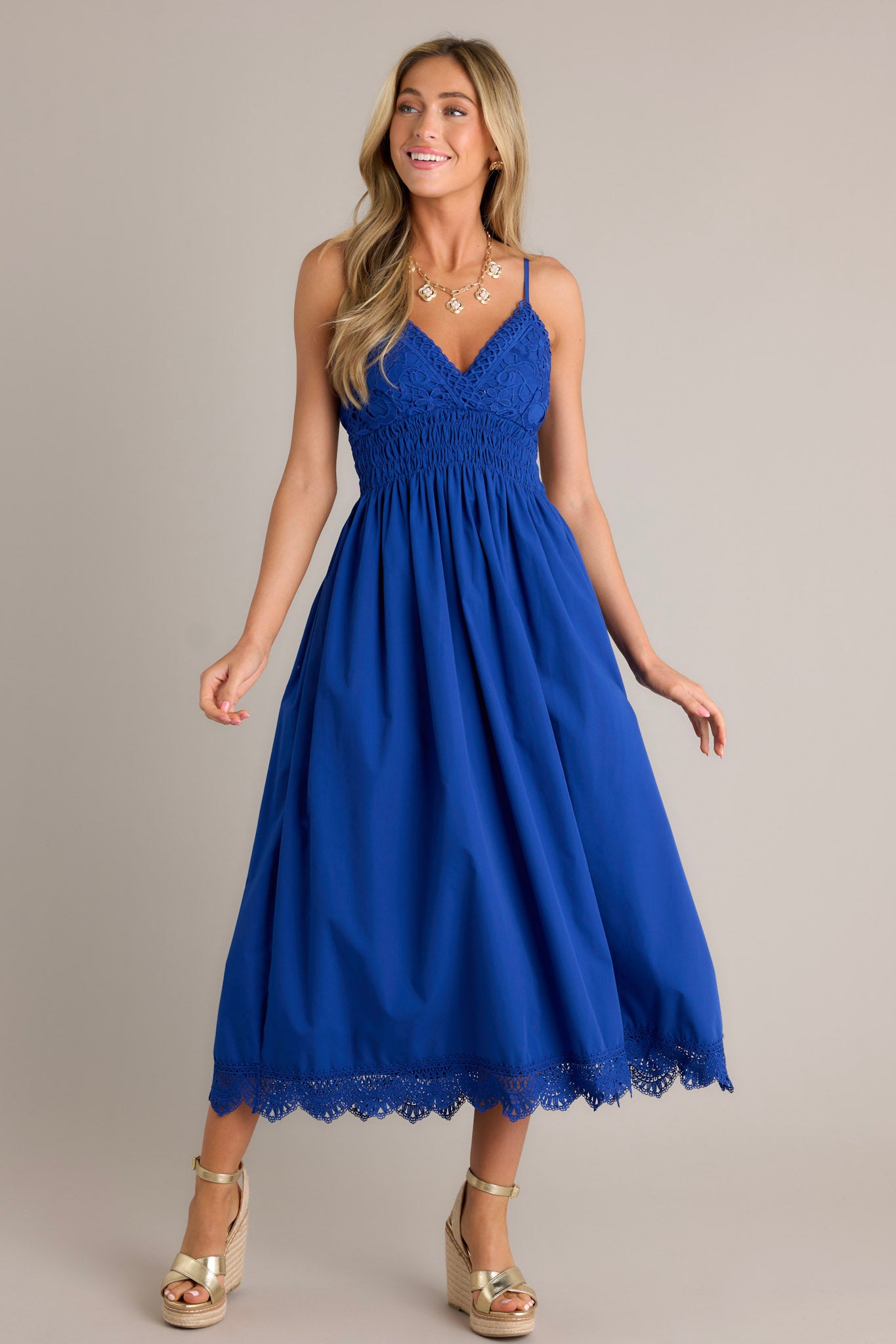 Action shot of a blue maxi dress displaying the fit and movement, highlighting the v-neckline, thin adjustable straps, lace bust, smocked waist & back, flowing silhouette, and lace hemline.