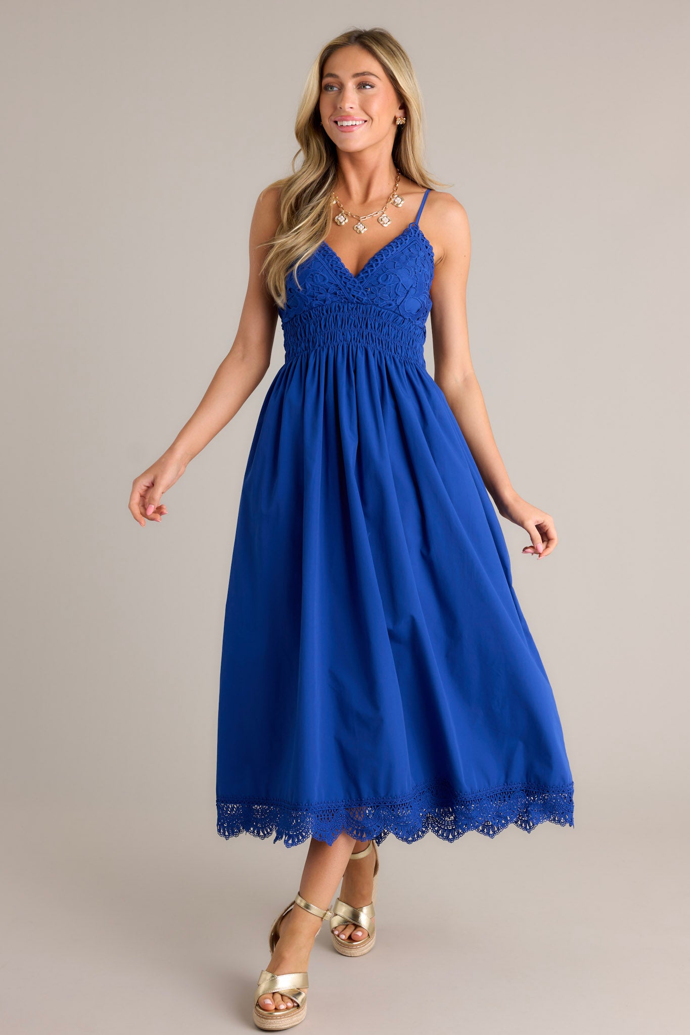 Full length view of a blue maxi dress with a v-neckline, thin adjustable straps, a lace bust, a fully smocked waist & back, a flowing silhouette, and a lace hemline